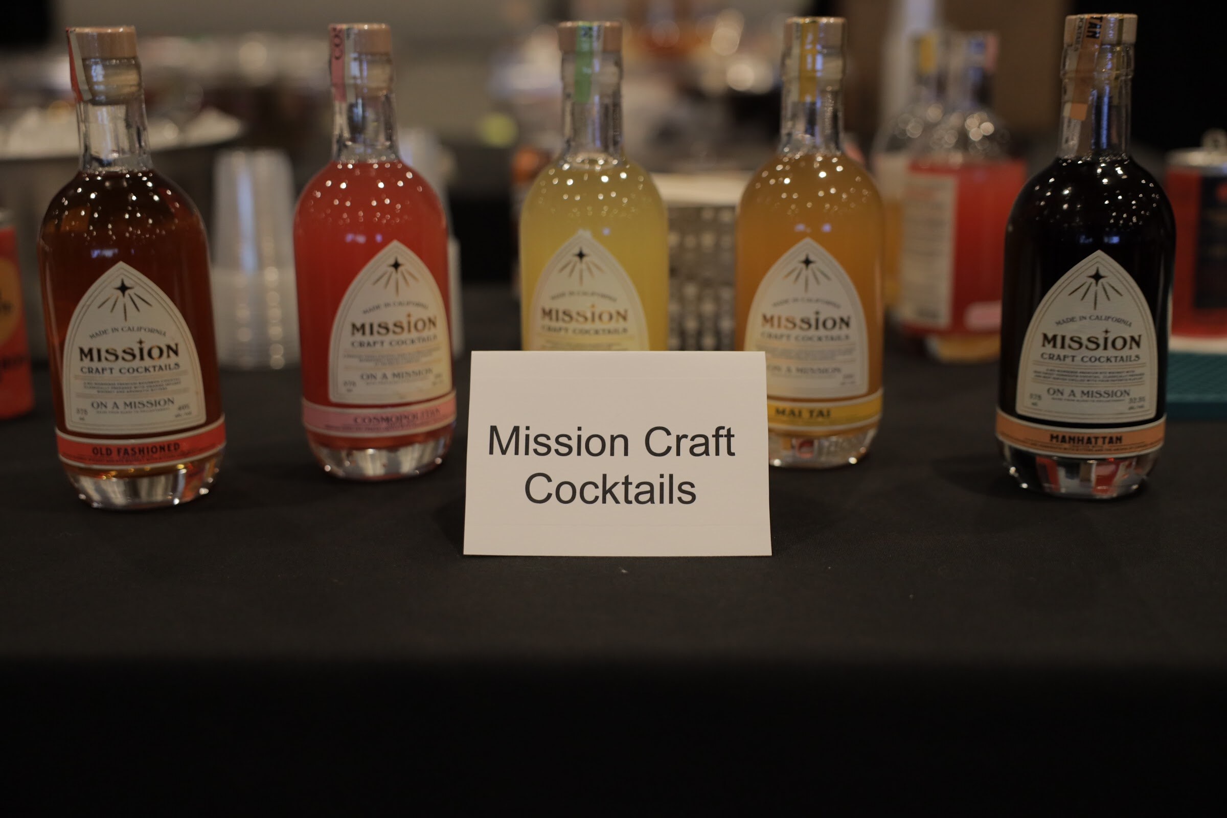 Five bottles of cocktails with a card reading Mission Craft Cocktails on a table.