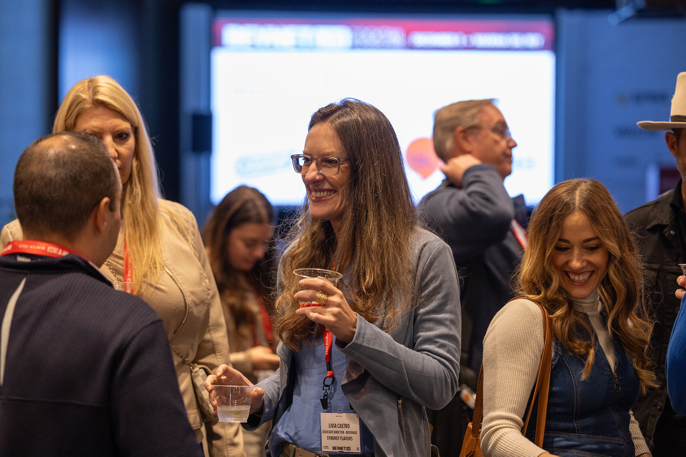 Several attendees in lanyards smile and talk with cups in their hands.