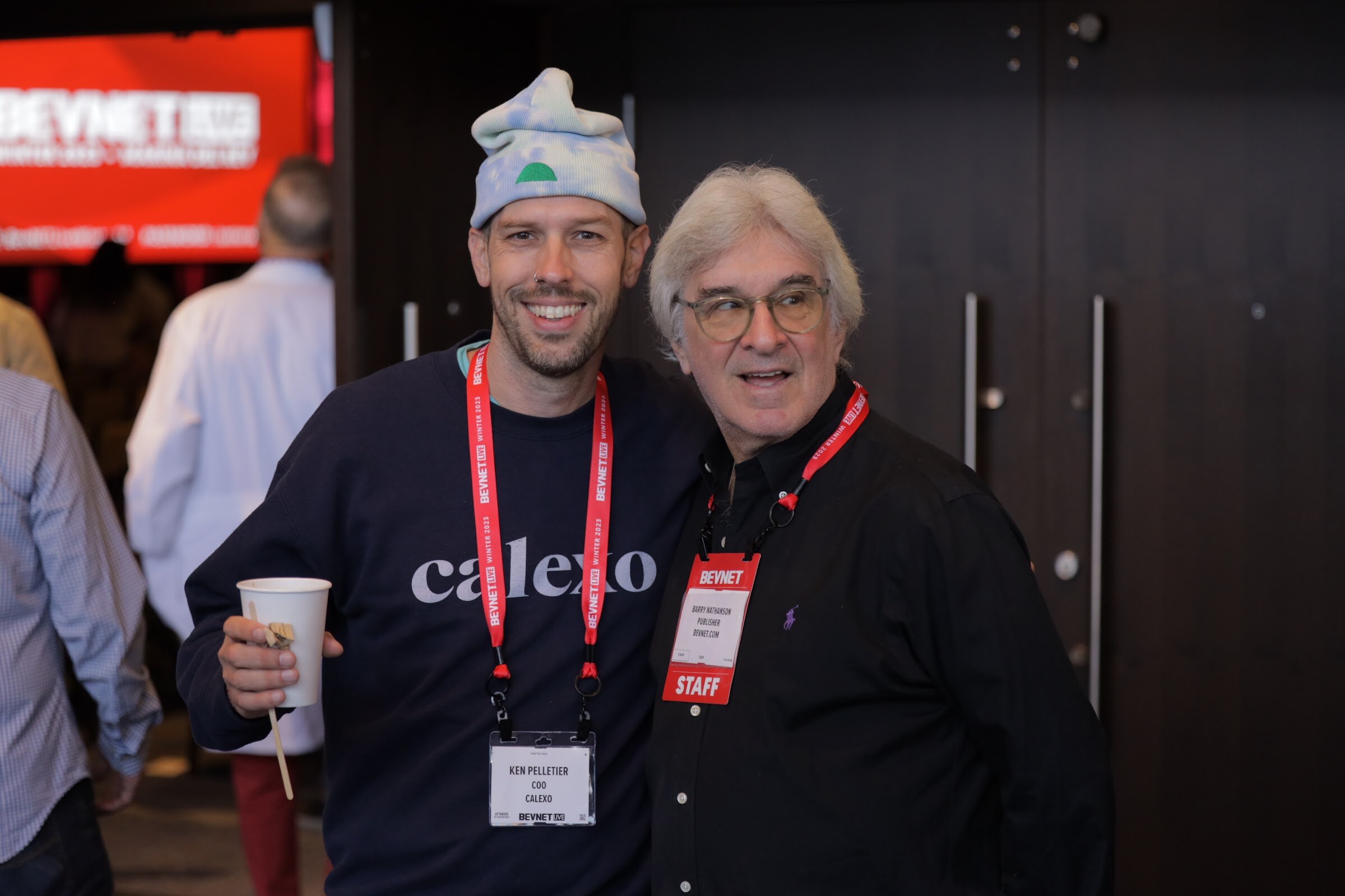 Two men with lanyards smile for the camera, one wearing a sweatshirt that reads calexo.