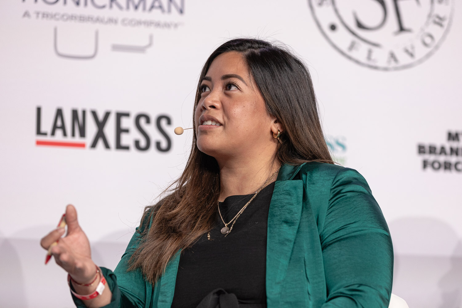 A woman in a green blazer speaks and gestures while looking up toward the stage.
