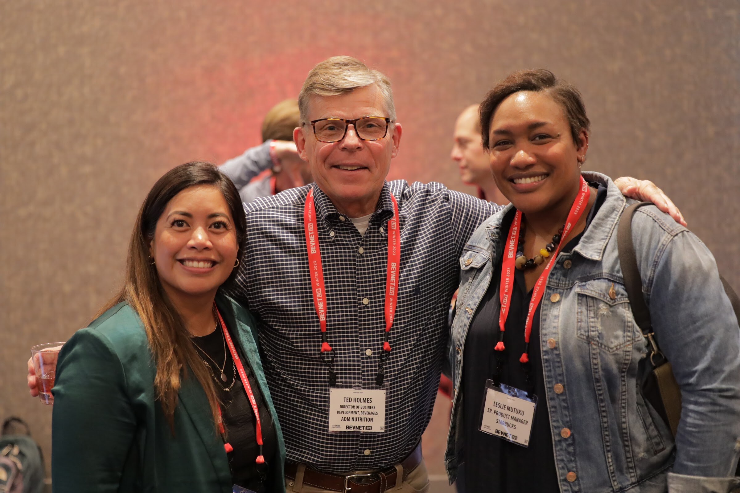 A woman in green and a man with glasses and a woman in a denim jacket pose smiling, all in lanyards.
