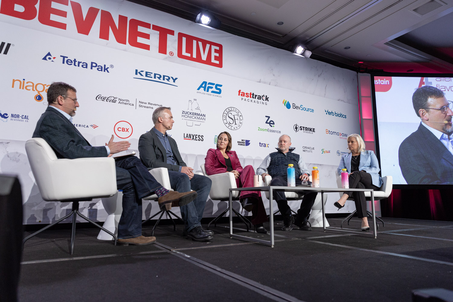 Five people sit on the stage under a BevNET Live sponsor wall with a screen at right.