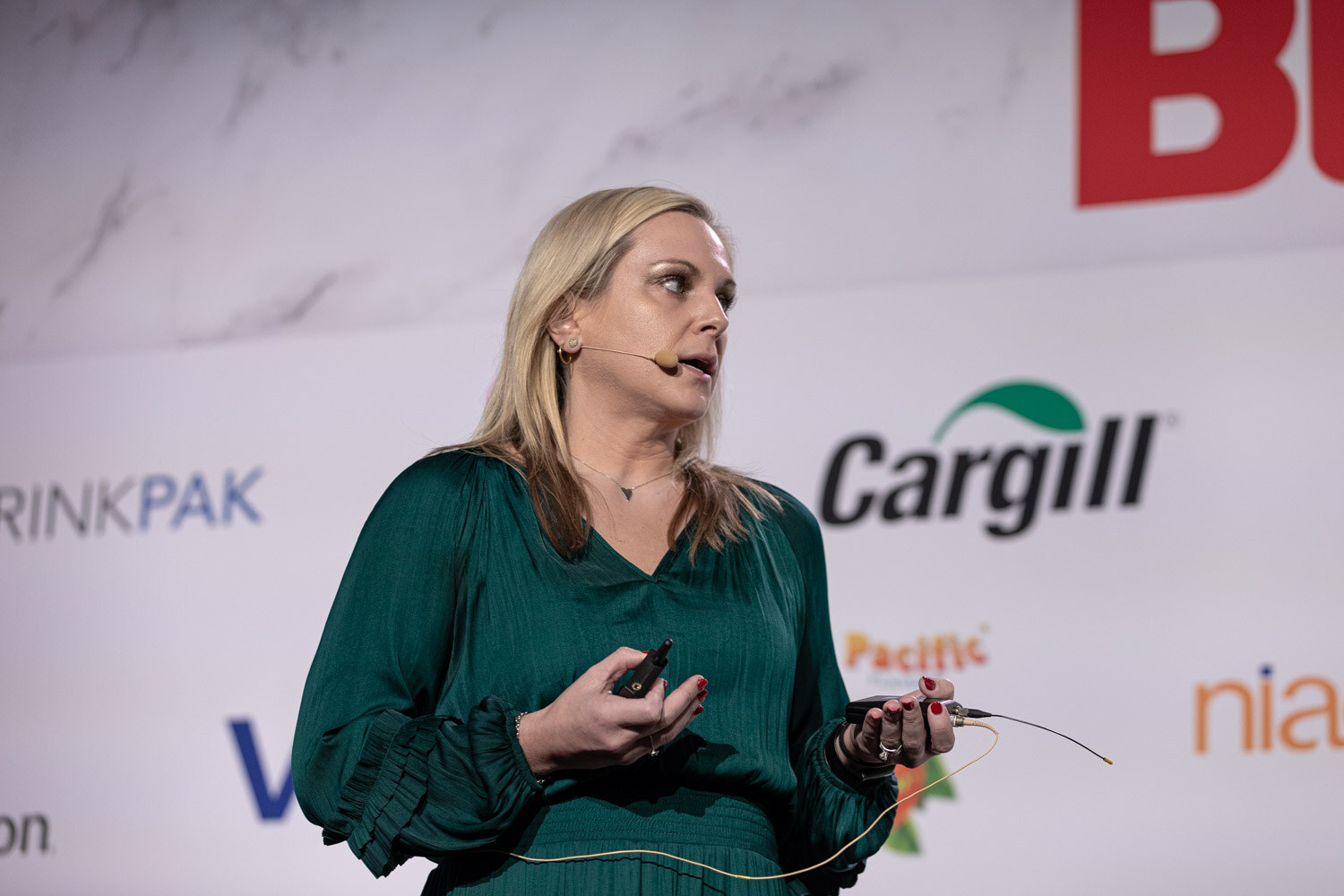 A woman with blond hair in a green dress holds a clicker and looks to the side.