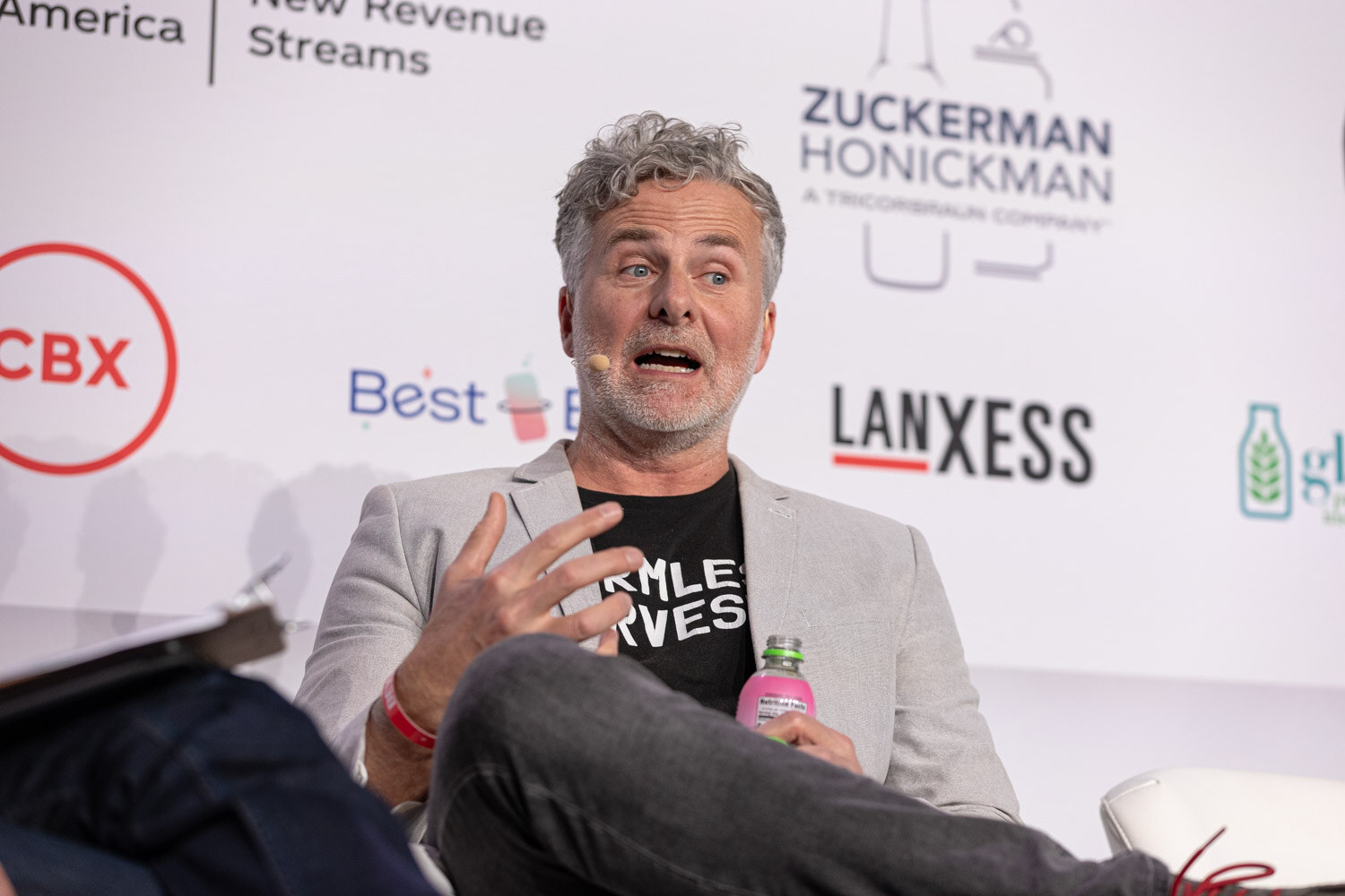 A man with gray hair in a gray blazer speaks in front of a CBX sponsor logo.