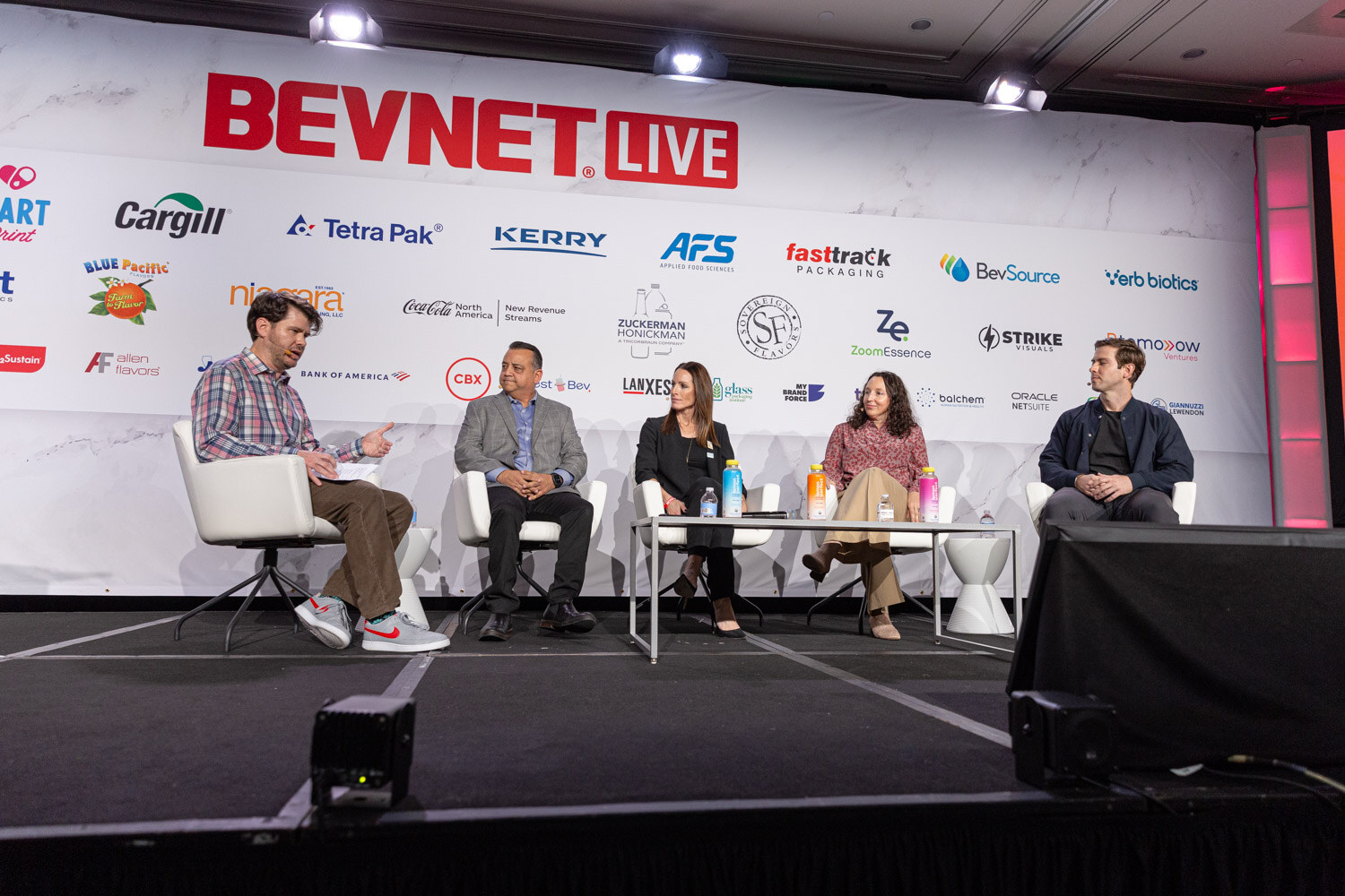 A wide shot of five people seated on a stage in front of a BevNET Live sponsor wall.