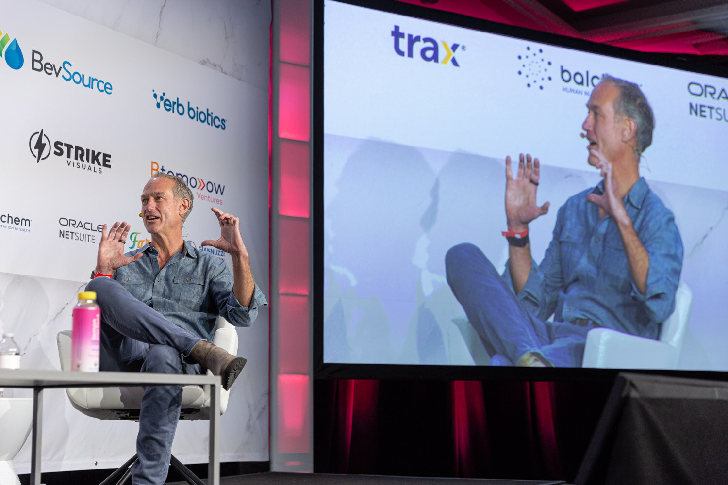 A stage with a screen showing a panelist and one panelist seated in front of it.
