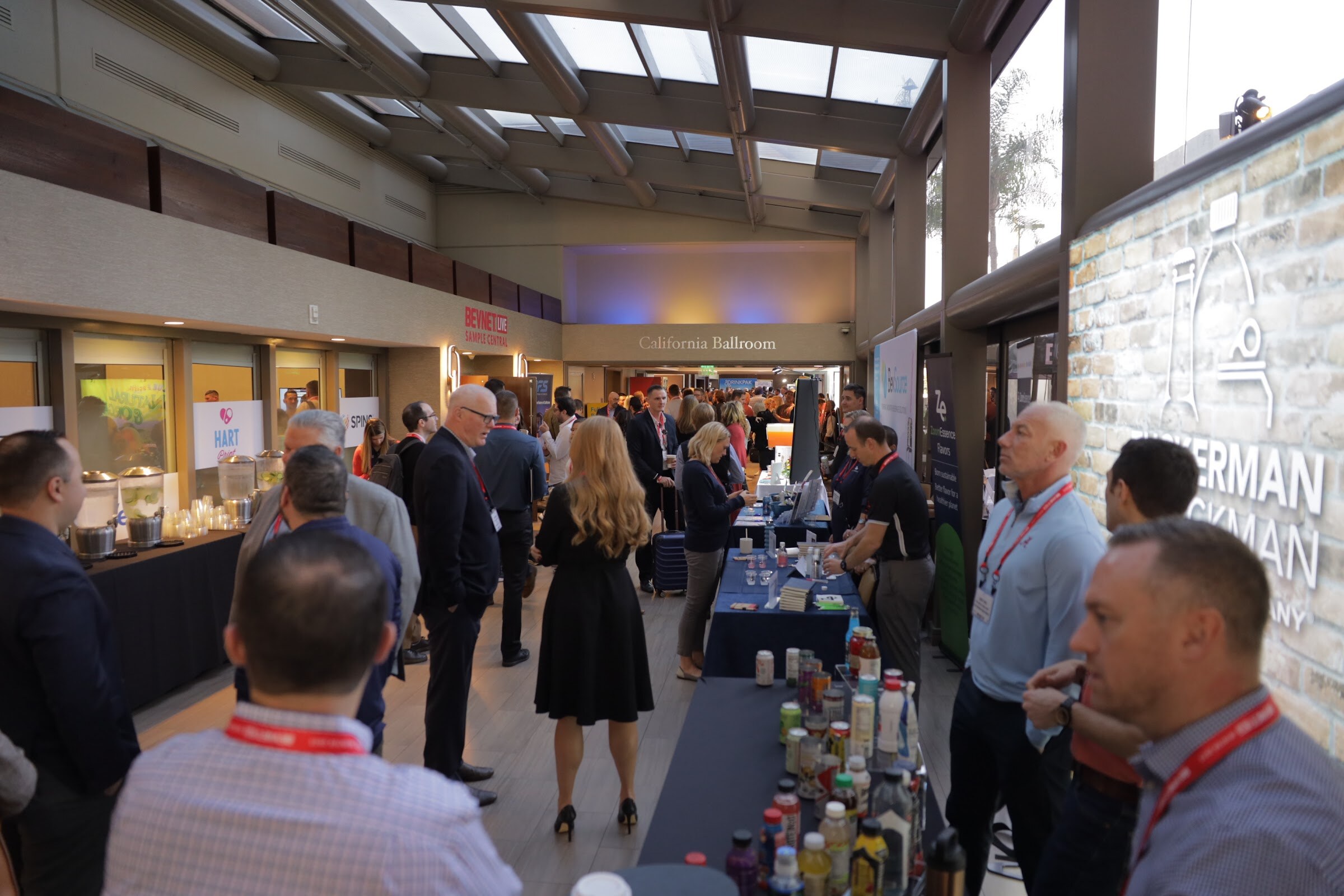 A hallway lined with tables of bottles and cans as attendees talk and sample.