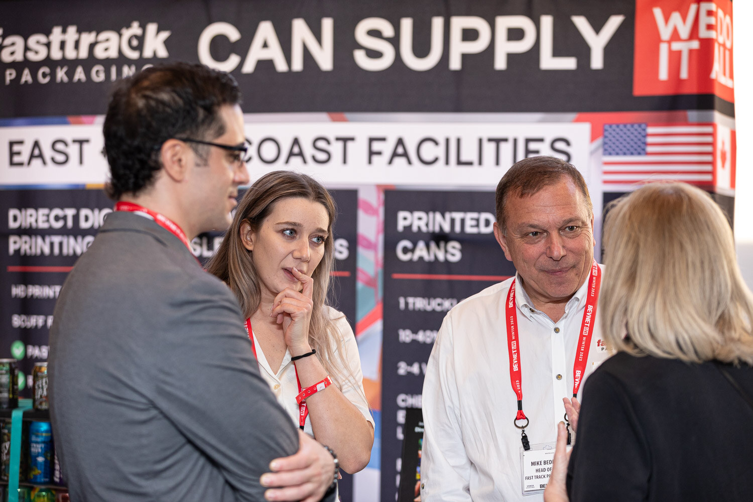 Attendees stand in front of a banner reading Fasttrack Can Supply with printed can samples.
