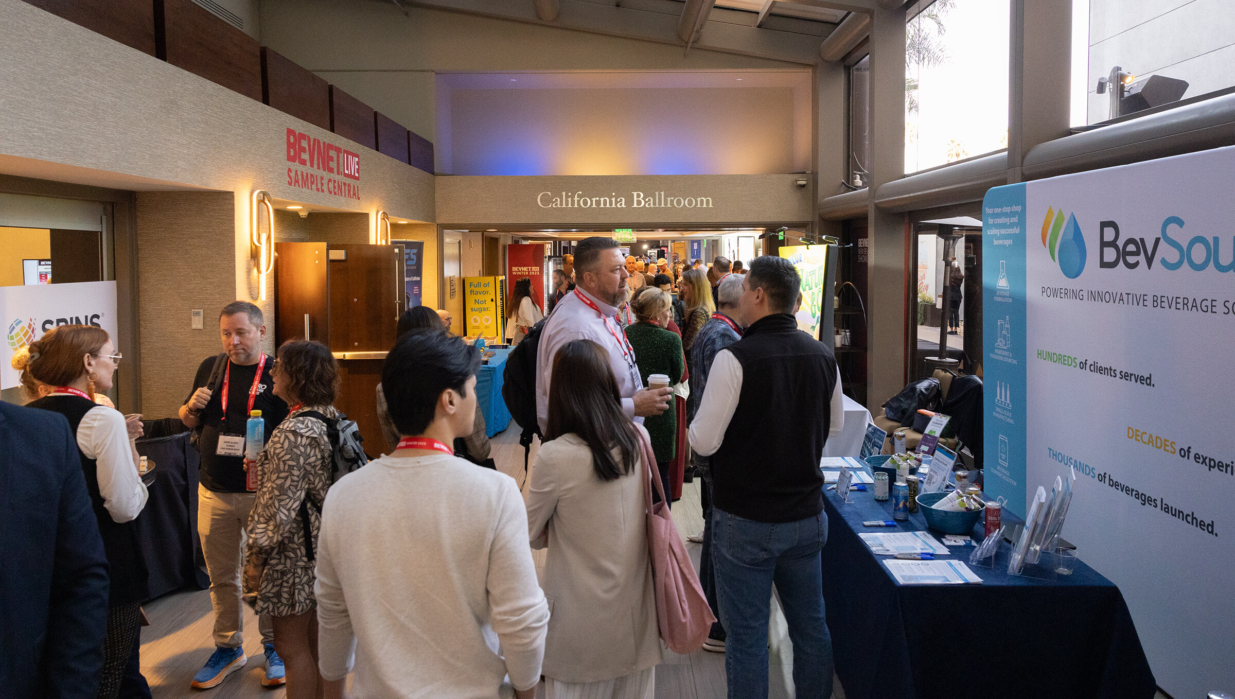 A busy covered hallway with exhibitor tables and attendees in lanyards.