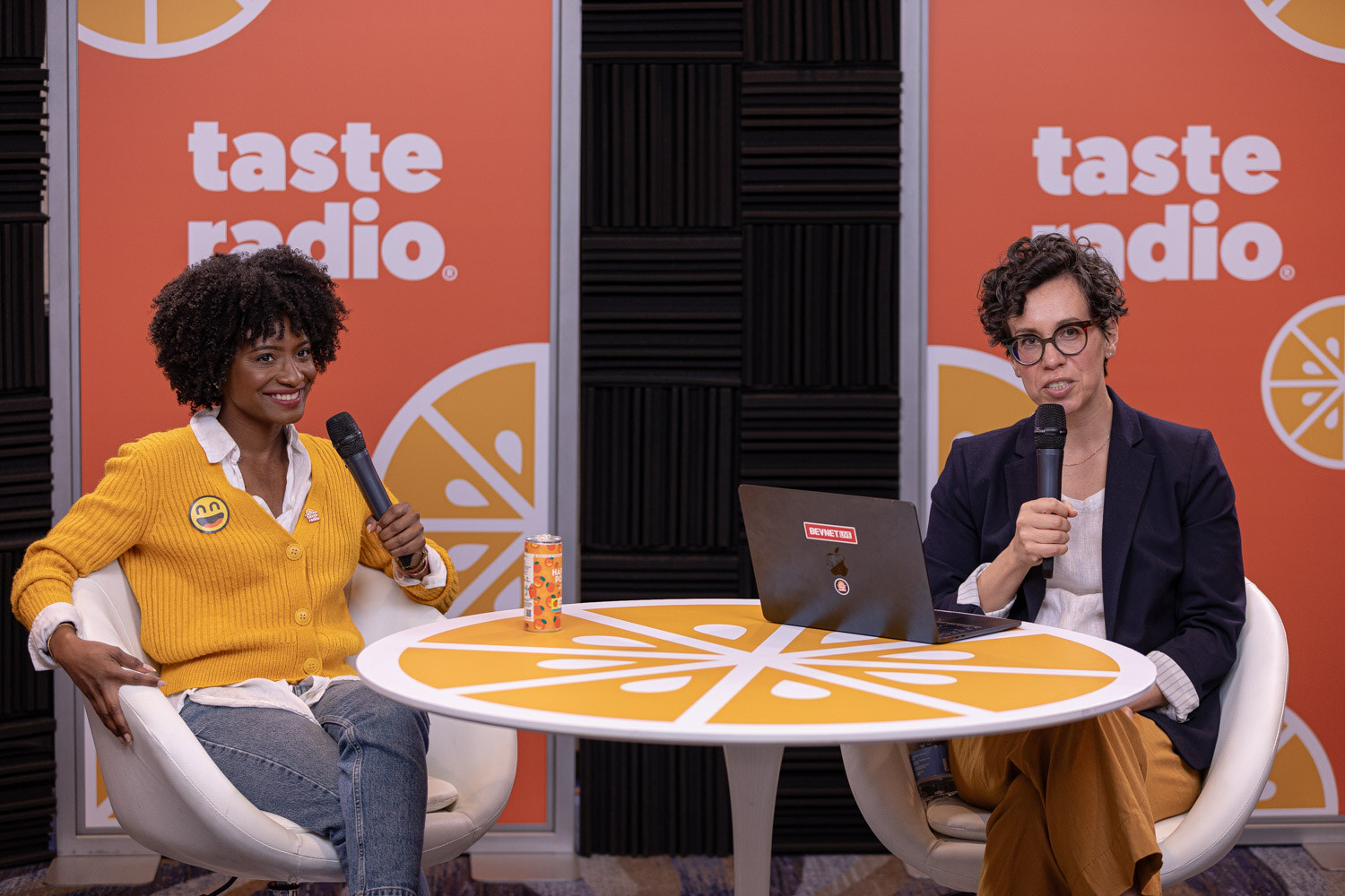 A woman in a yellow cardigan and a woman with short curly hair at a round table with a laptop.