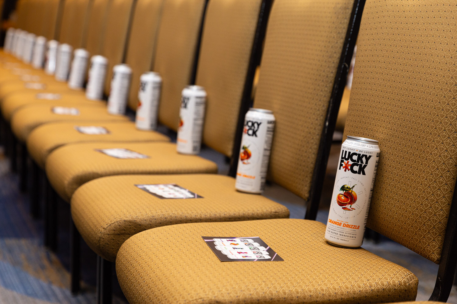 A row of gold theater chairs with beverage cans and small cards placed on the seats.