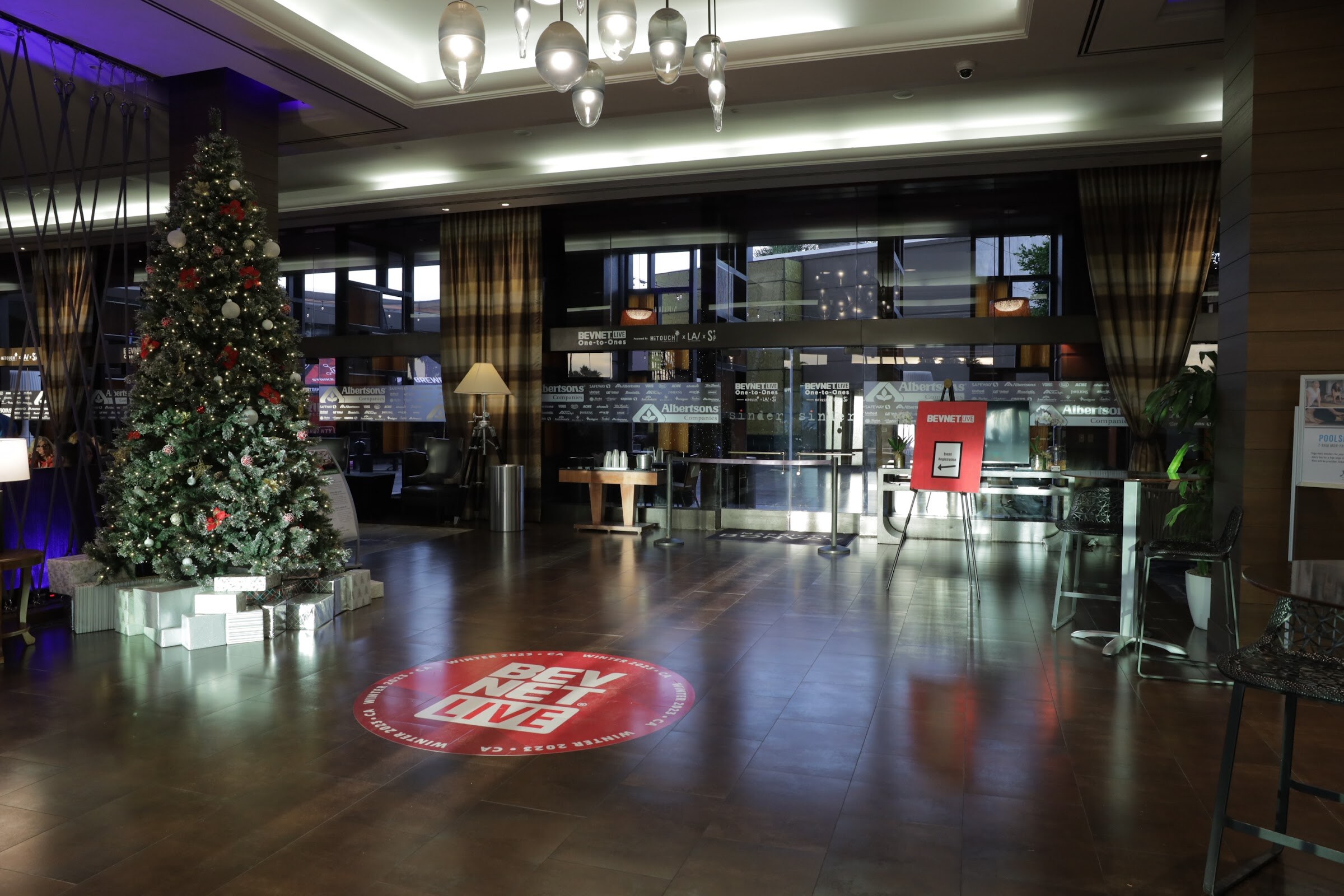 An empty hotel lobby with a decorated Christmas tree and a red BevNET Live logo projected on the floor.
