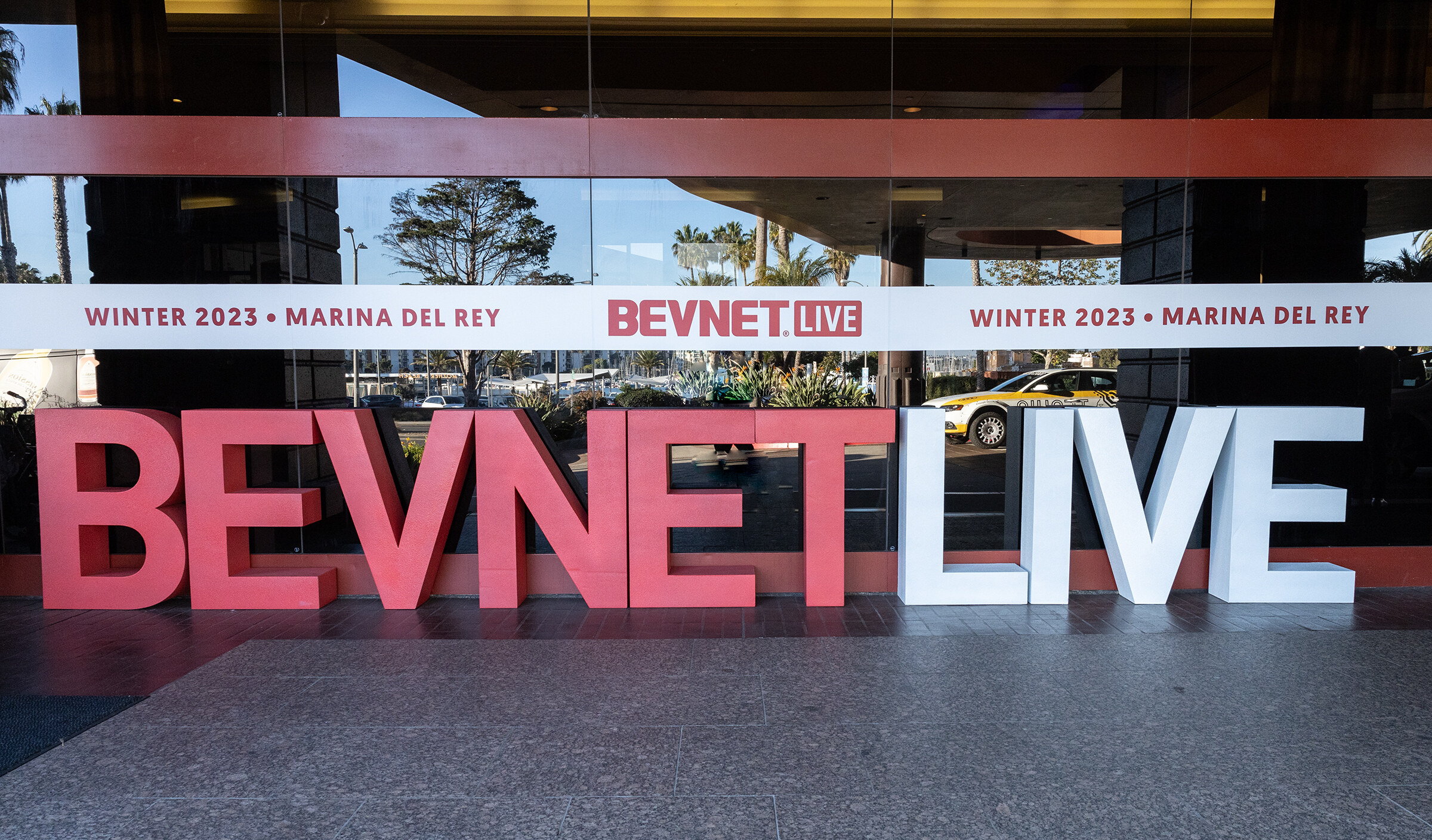Tall letters spelling BEVNET LIVE stand outside a glass entrance with a Winter 2023 Marina del Rey banner above.