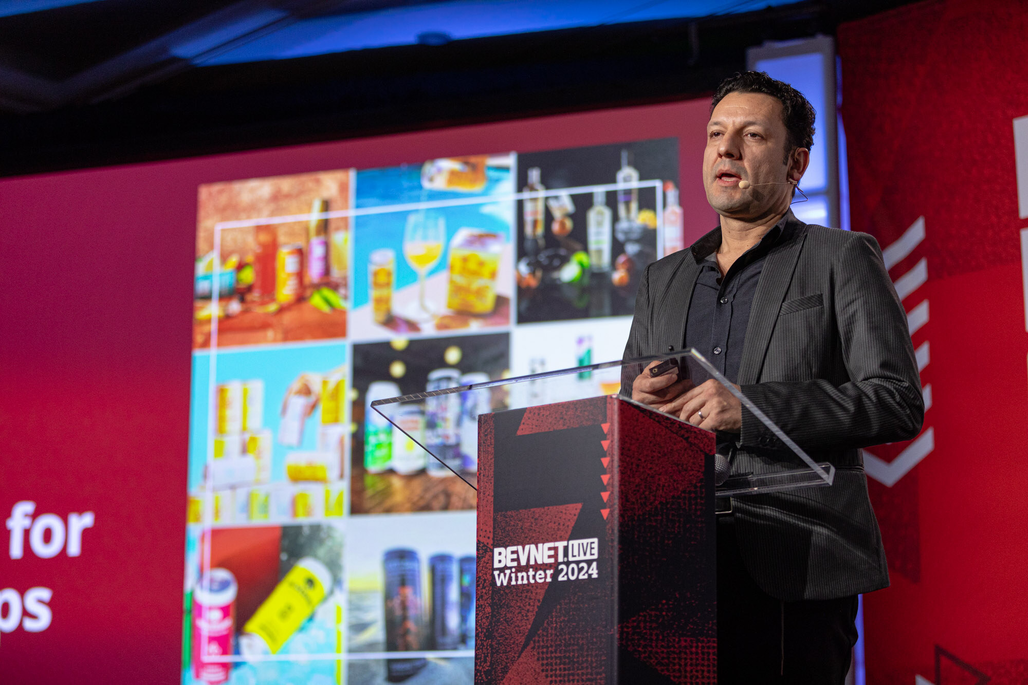 Man in a dark jacket speaks at a podium in front of a screen full of product images.