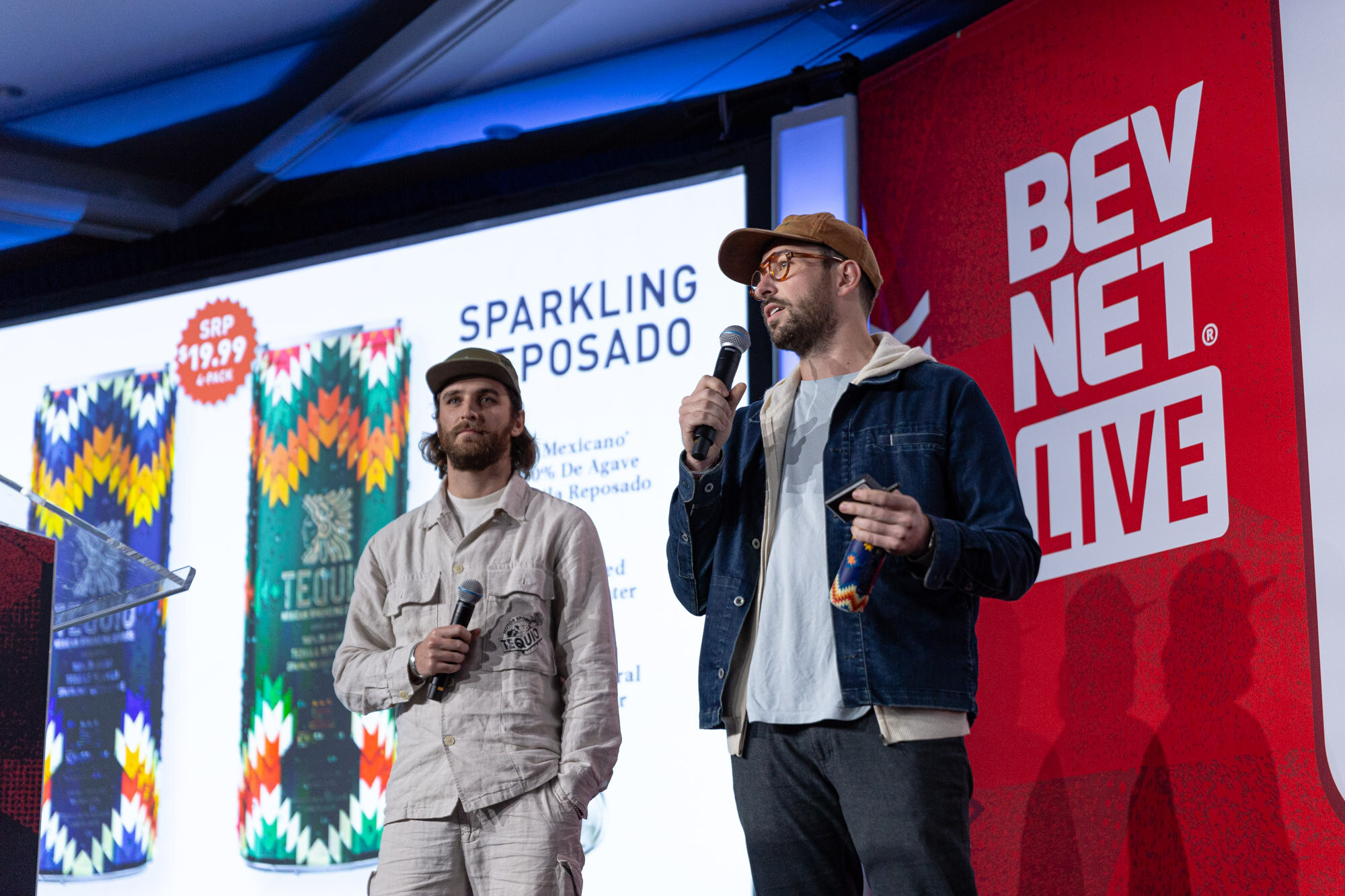 Two men stand in front of a Sparkling Reposado slide with cans decorated in colorful patterns.