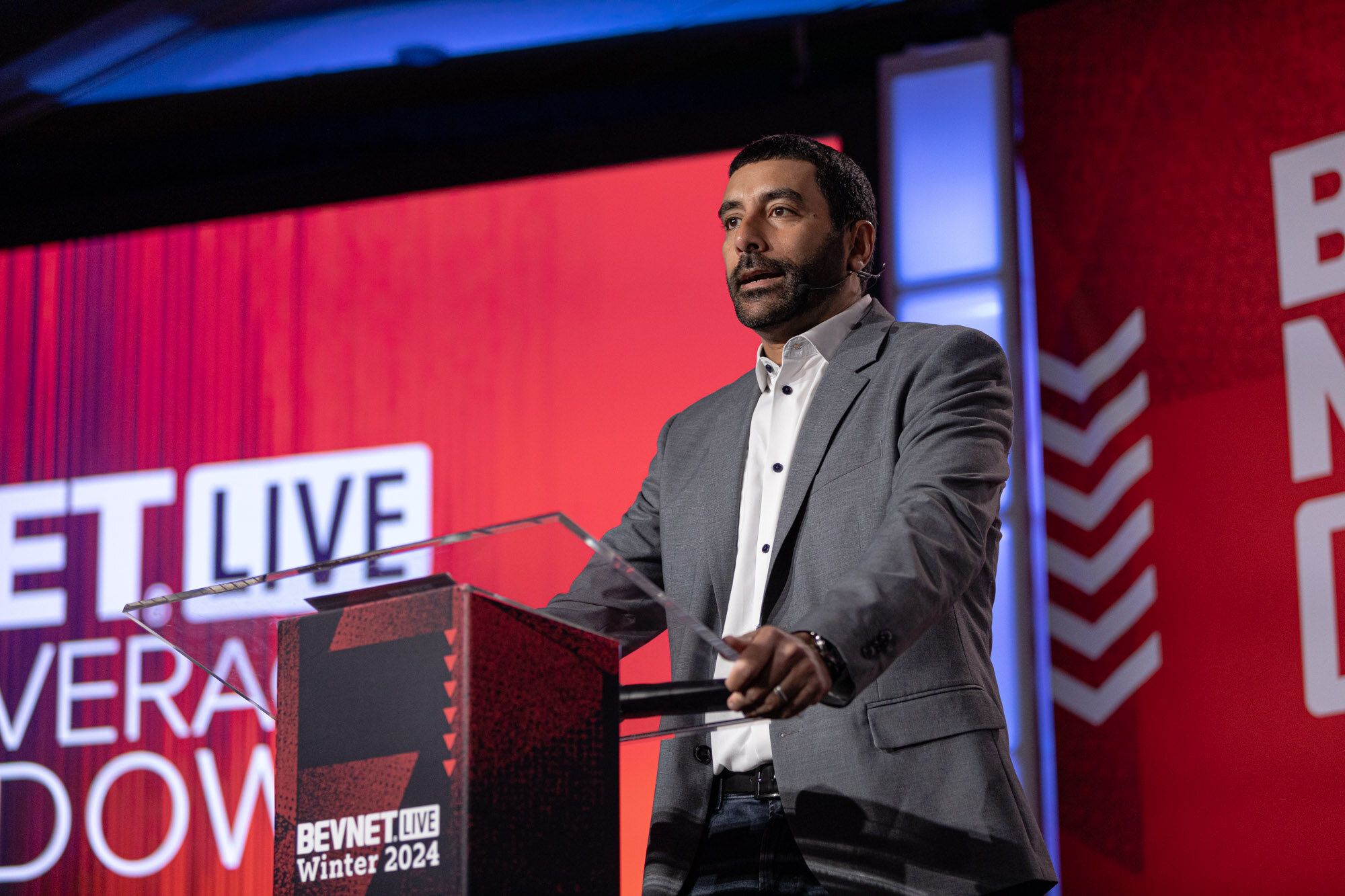 Man in a gray blazer speaks at a podium that reads BevNET Live Winter 2024 next to a New Beverage Showdown sign.