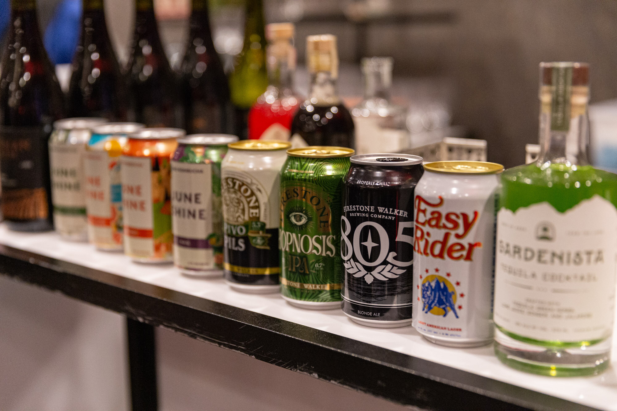A shelf holds cans and spirit bottles including Gardenista tequila cocktail, Easy Rider and 805.