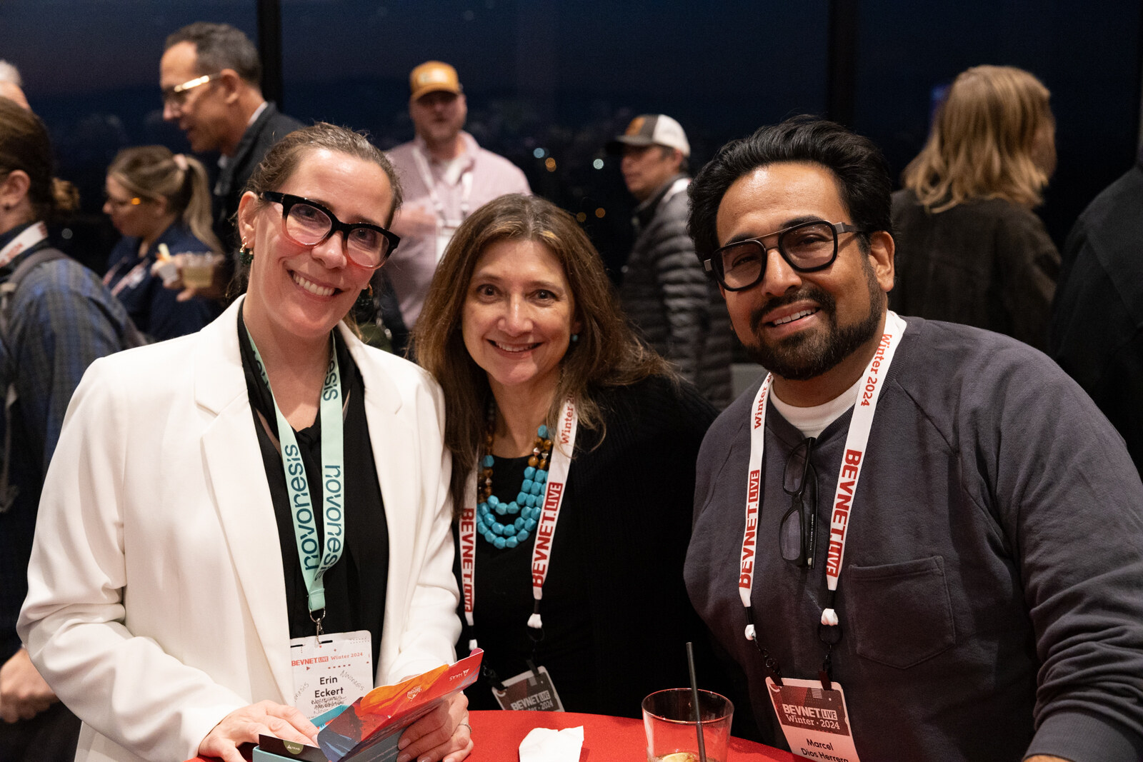 Two women and a man with glasses and BevNET Live lanyards smile and pose closely together.