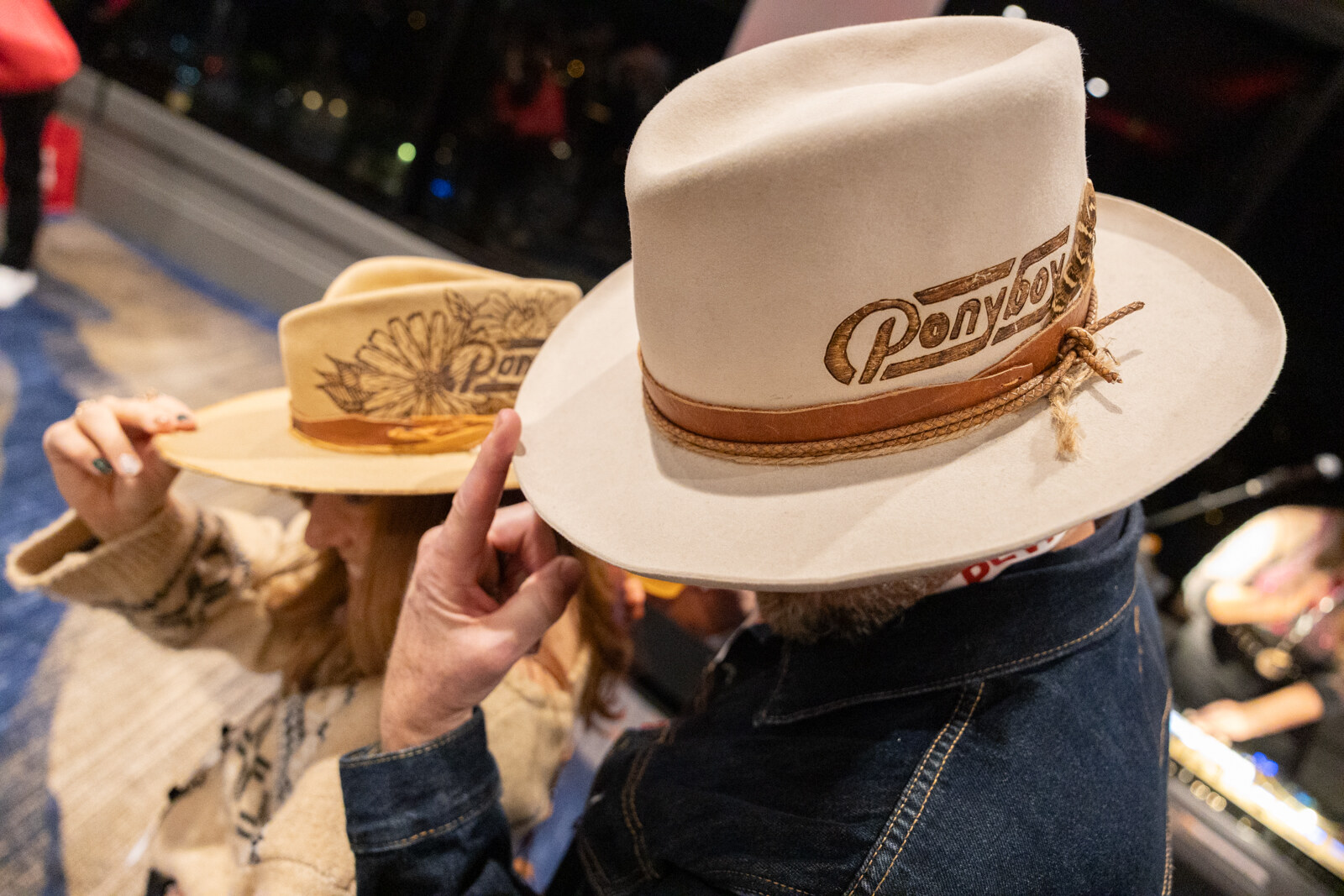 Close-up of a hand adjusting a cream hat with Ponyboy lettering on its band.