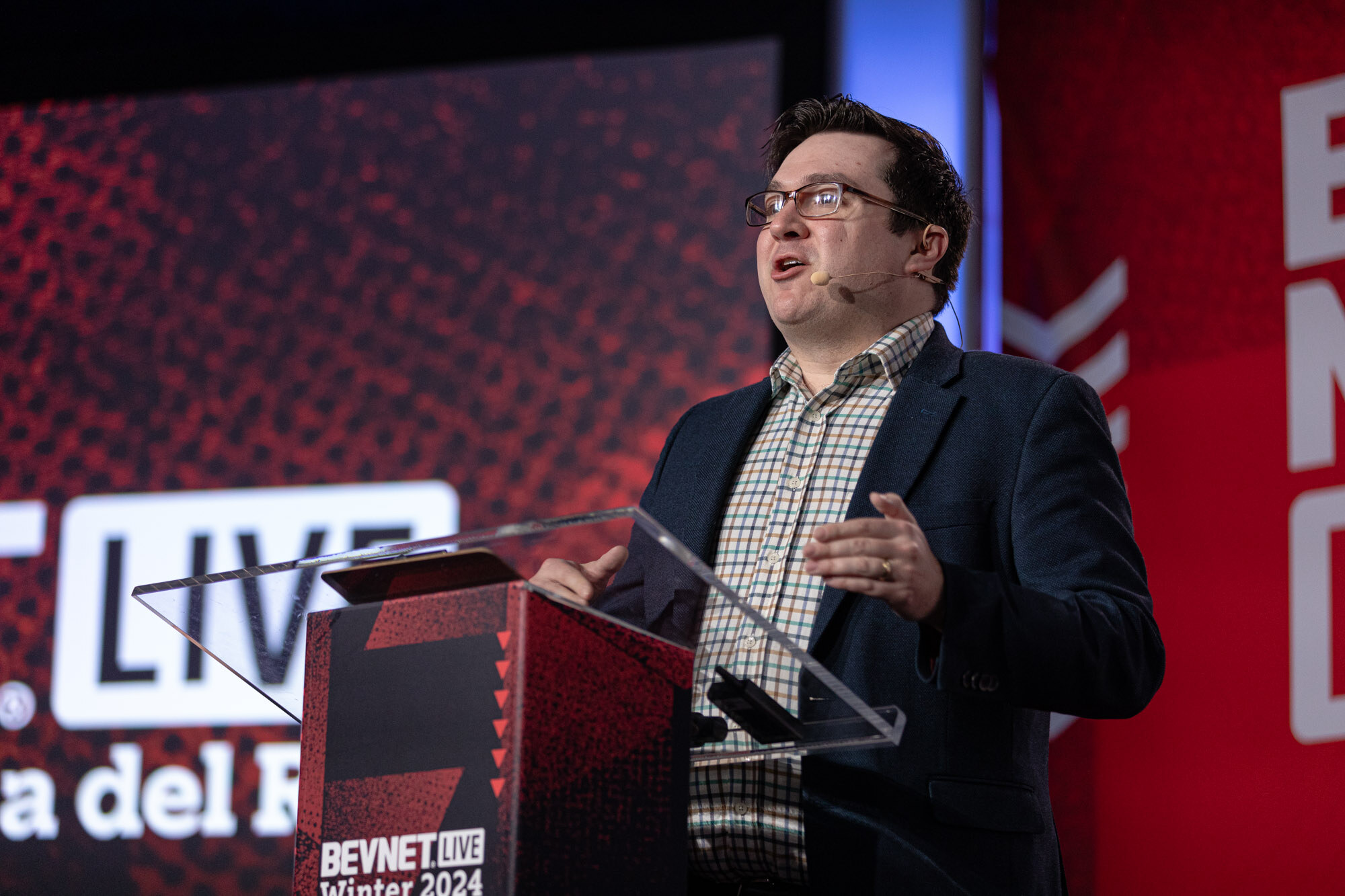 Man with glasses in a navy blazer speaks at a lectern marked BevNET Live Winter 2024.