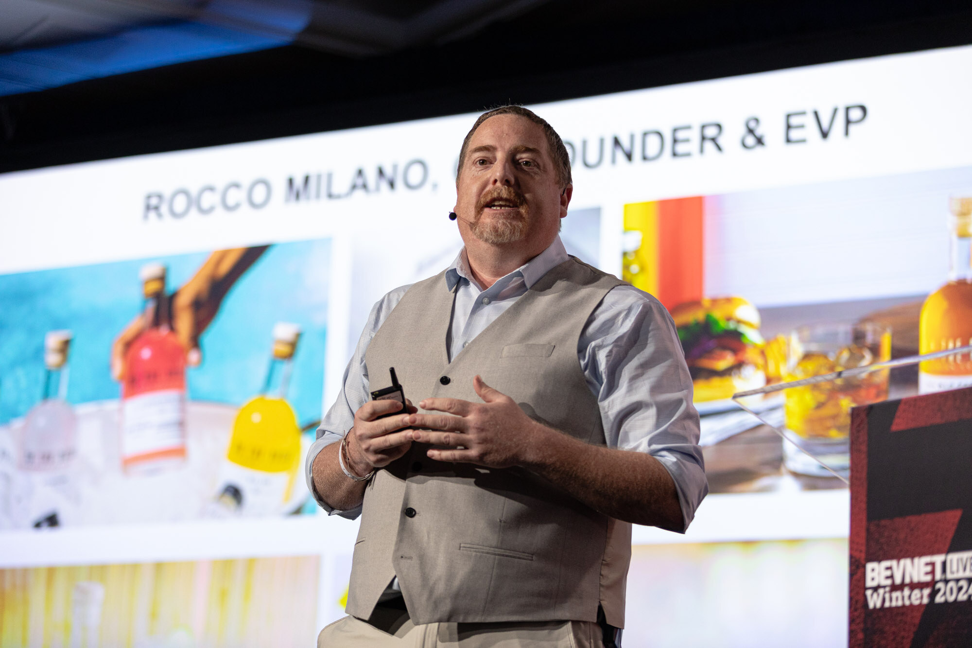 Man in a vest and glasses gestures in front of a slide with cocktail bottles and a title.