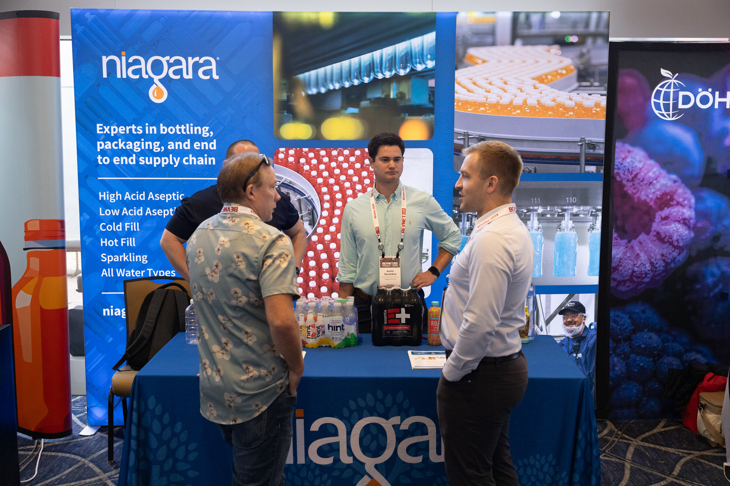 Several men stand at a blue table in front of a Niagara banner that reads Experts in bottling, packaging, and end to end supply chain.