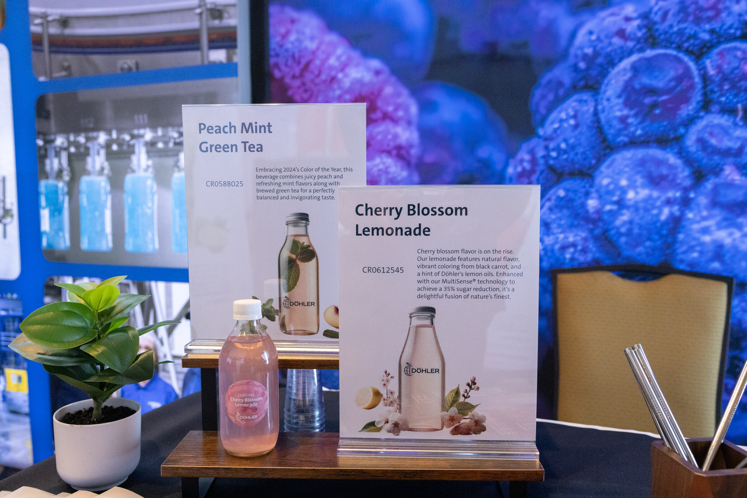 Two tags reading Peach Mint Green Tea and Cherry Blossom Lemonade next to bottles on a table in front of a blue Dohler backdrop.