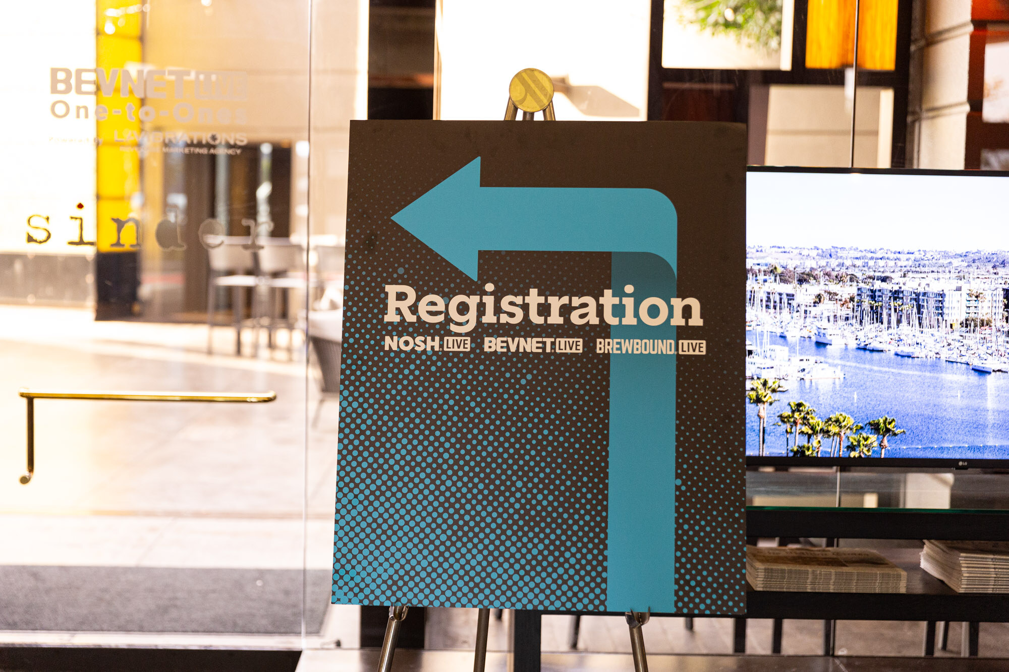 Sign with an arrow reading Registration with the three event logos in front of a window with a marina view.