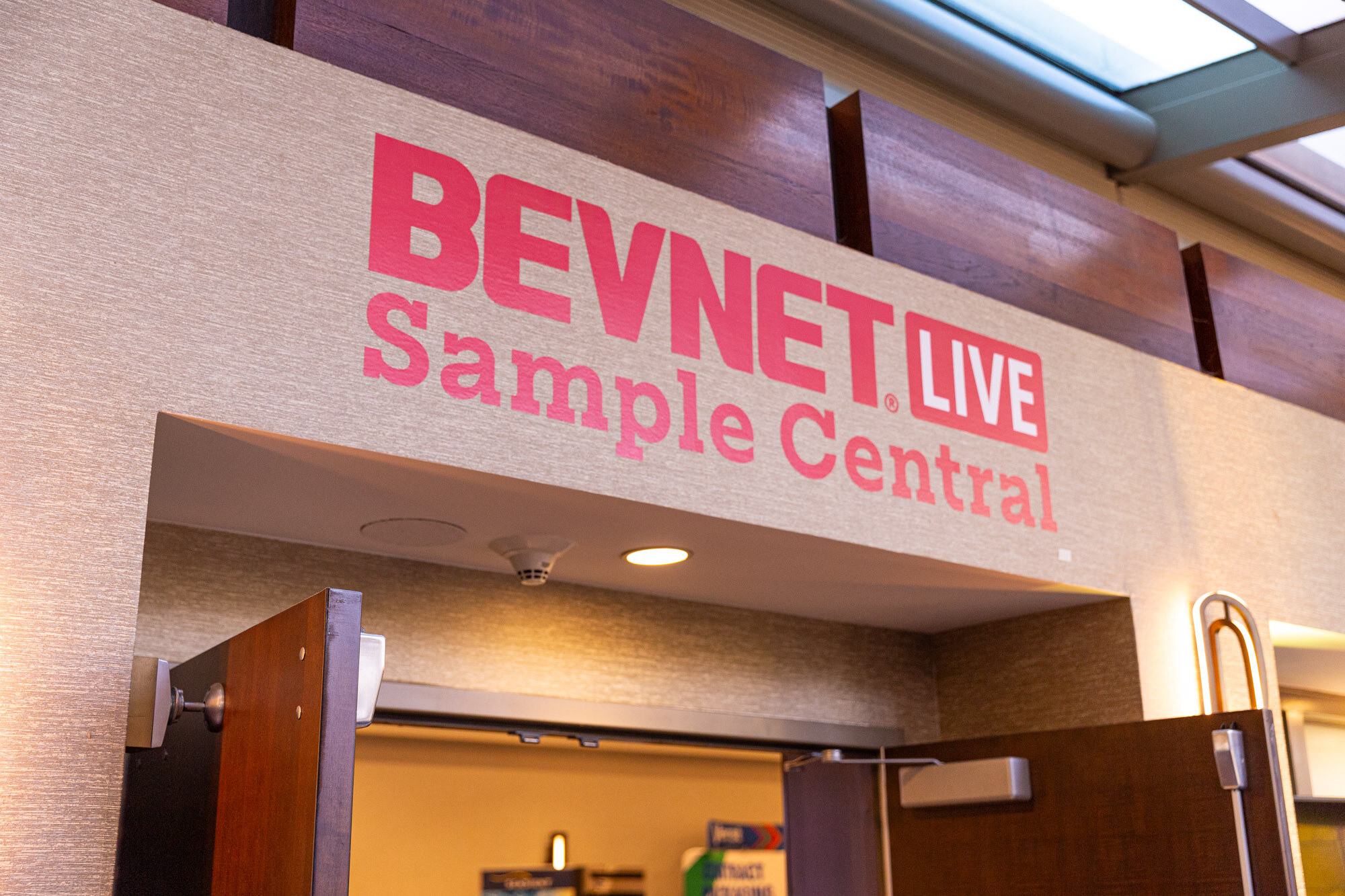 Sign on a wall reading BEVNET LIVE Sample Central above a doorway.