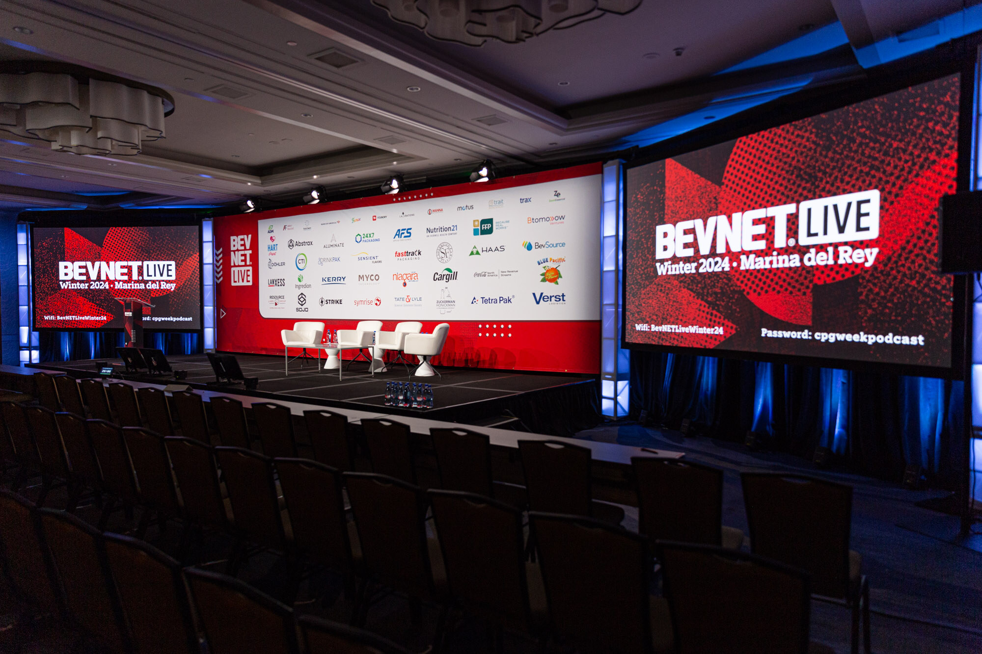Stage with two large red screens reading BevNET Live Winter 2024 Marina del Rey and rows of empty chairs.