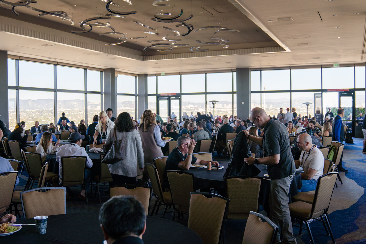 Wide view of attendees seated at round tables in a ballroom with large windows and a view of the city.