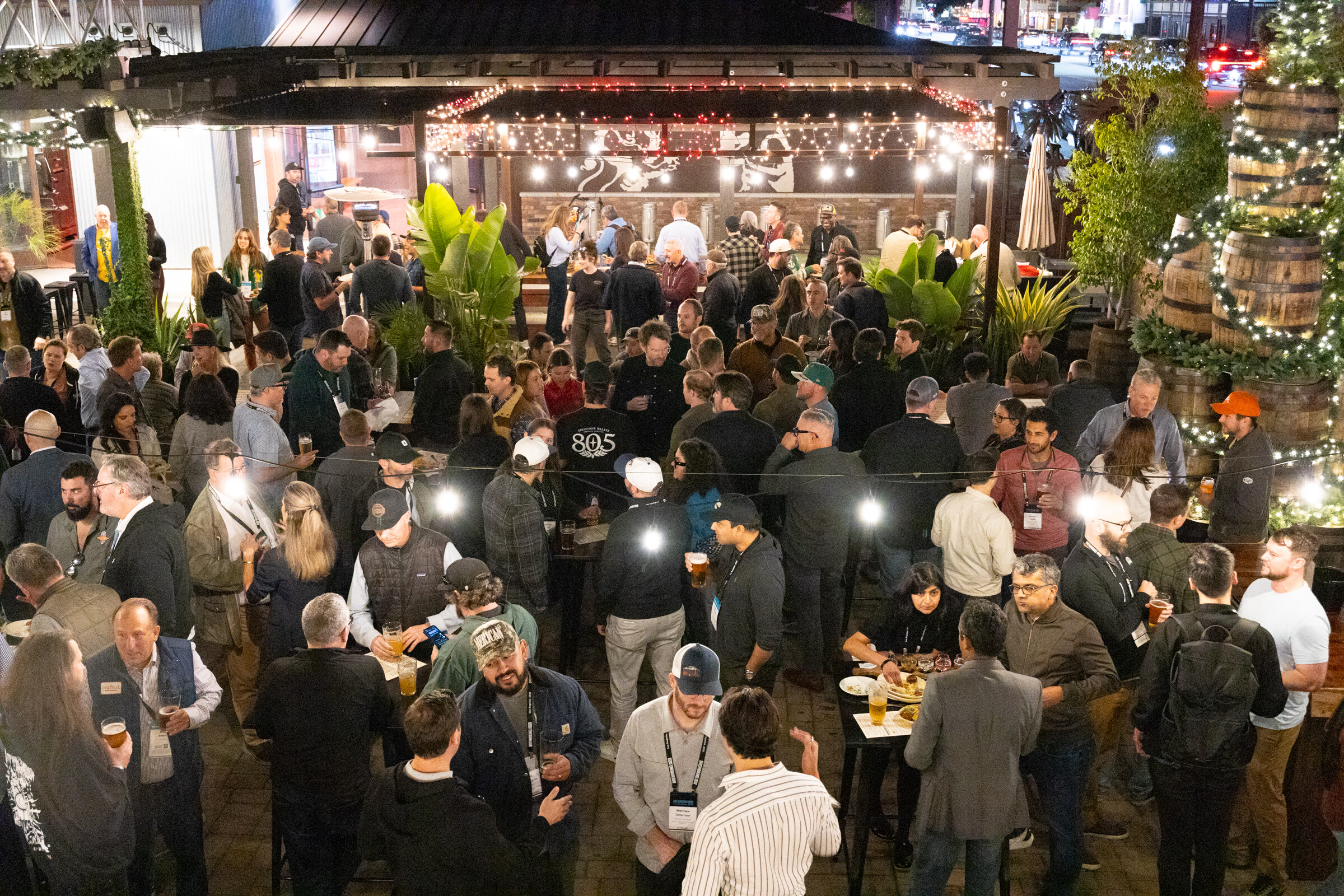 Aerial view of attendees with beers on a patio decorated with string lights, barrels and a Christmas tree.