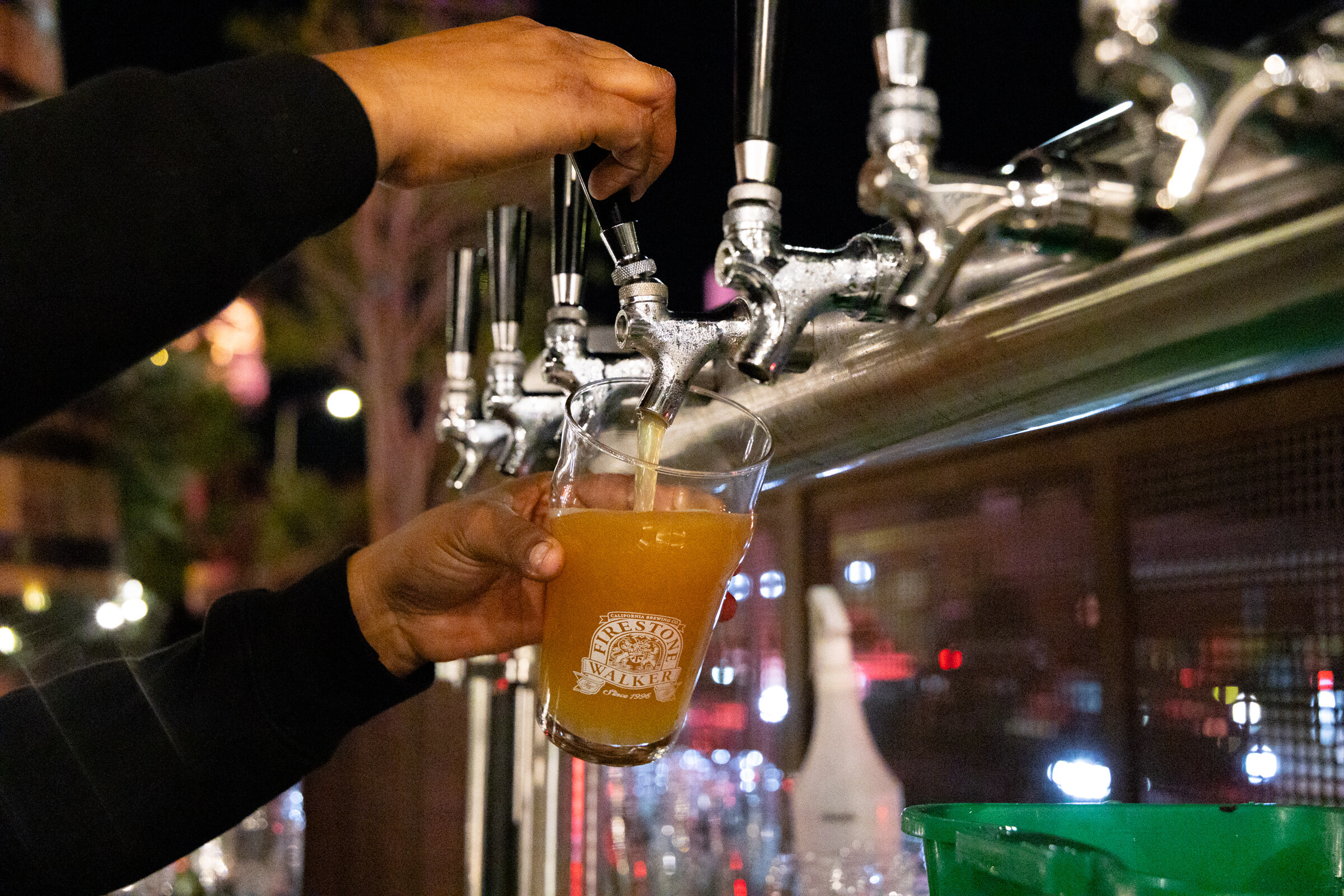 Hand pouring a golden beer into a Firestone Walker glass from a row of tap handles.