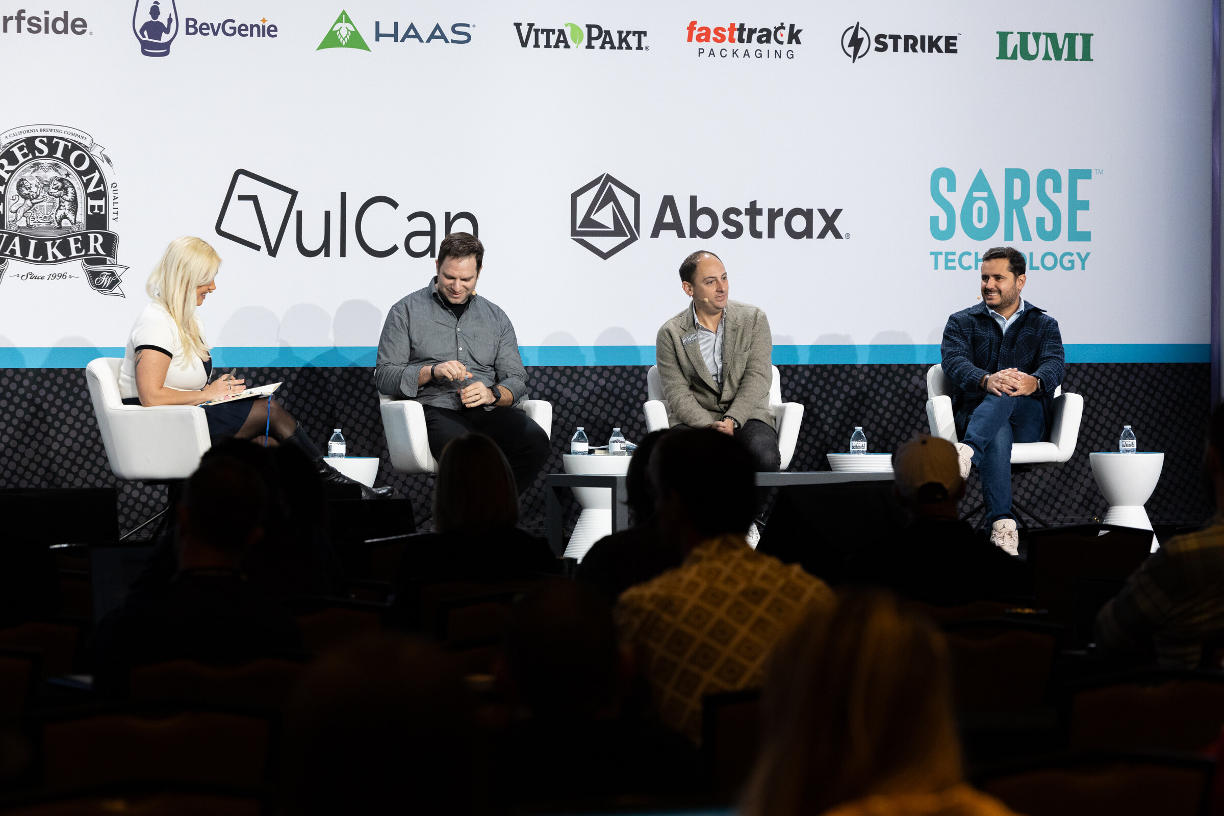 Four people seated on white chairs on a stage in front of a sponsor wall including VulCan, Abstrax and Sorse Technology, with audience heads in the foreground.