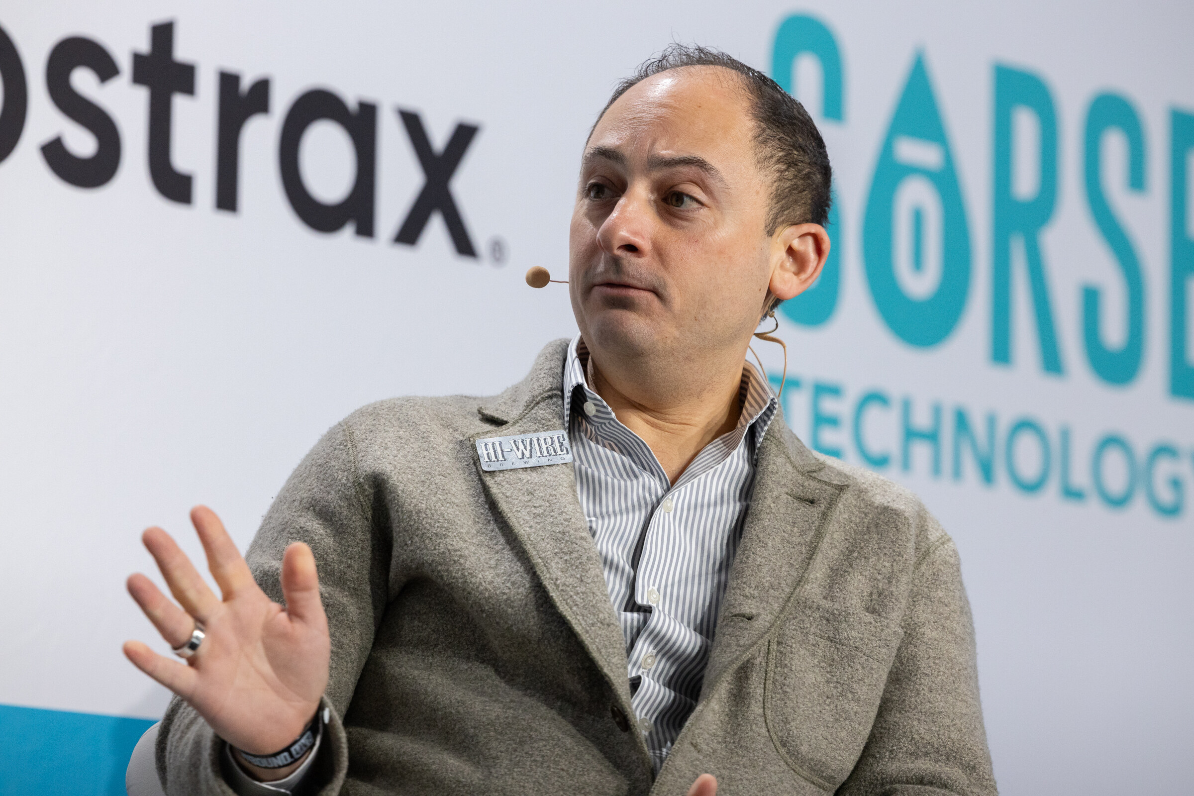 Man in a gray blazer and striped shirt gesturing with one hand in front of a Sorse Technology logo.