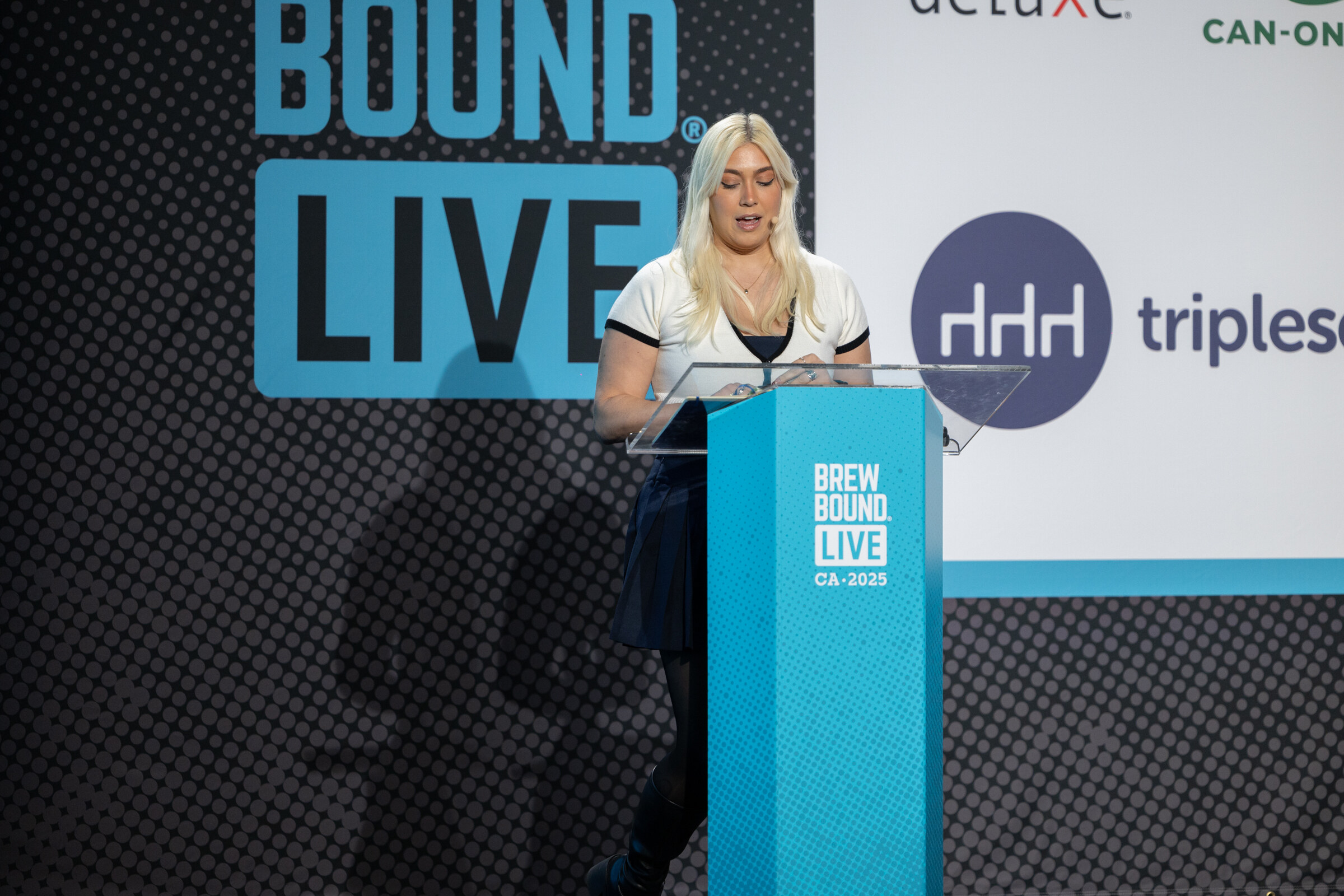 Woman with long blond hair standing at a teal Brewbound Live podium in front of a Tripleseat logo.