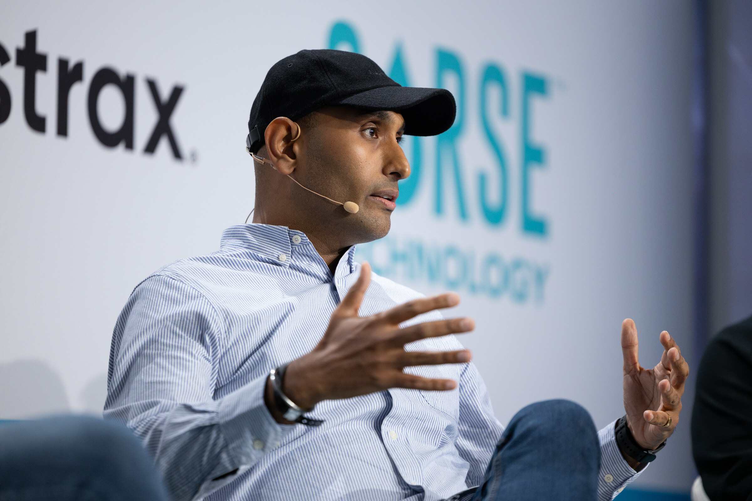 Man in a black cap and light striped shirt gesturing with both hands in front of Abstrax and Sorse logos.