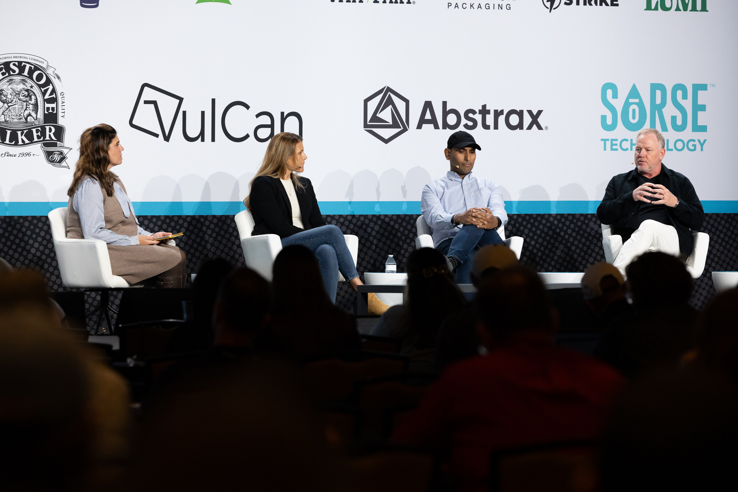 Four people seated on white chairs on stage in front of a sponsor wall with Firestone Walker, VulCan, Abstrax and Sorse logos.