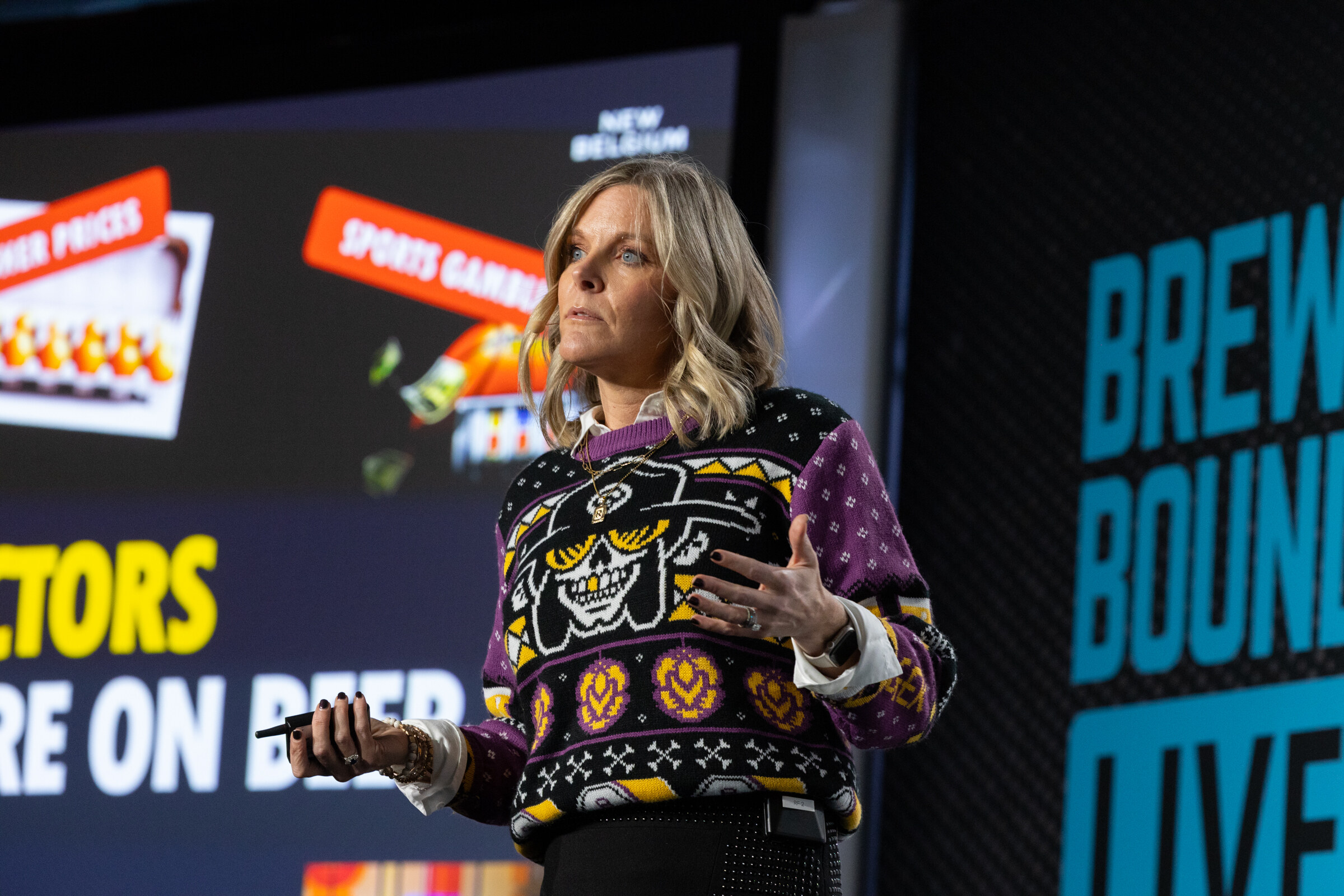 Woman in a patterned sweater speaking in front of a screen with slot machine graphics and a New Belgium logo.