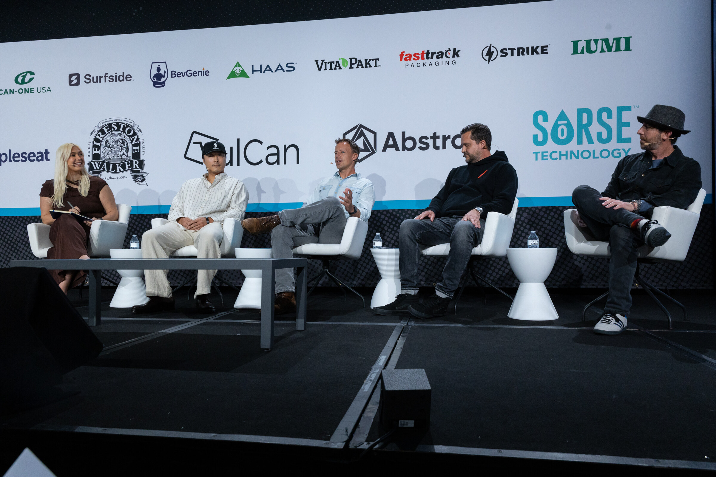 Five people seated on white chairs on a stage in front of a sponsor wall including VulCan, Abstrax and Sorse Technology.