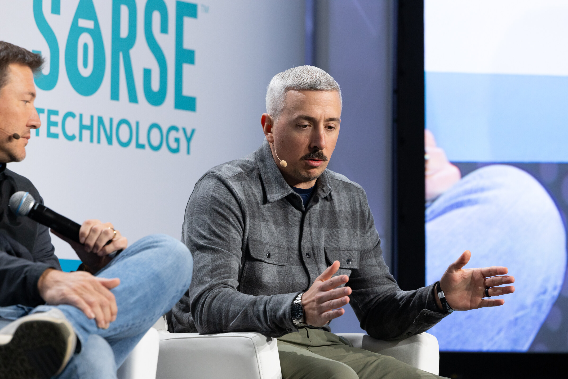Man with gray hair and a mustache in a plaid shirt gesturing while seated, with a Sorse Technology logo behind him.