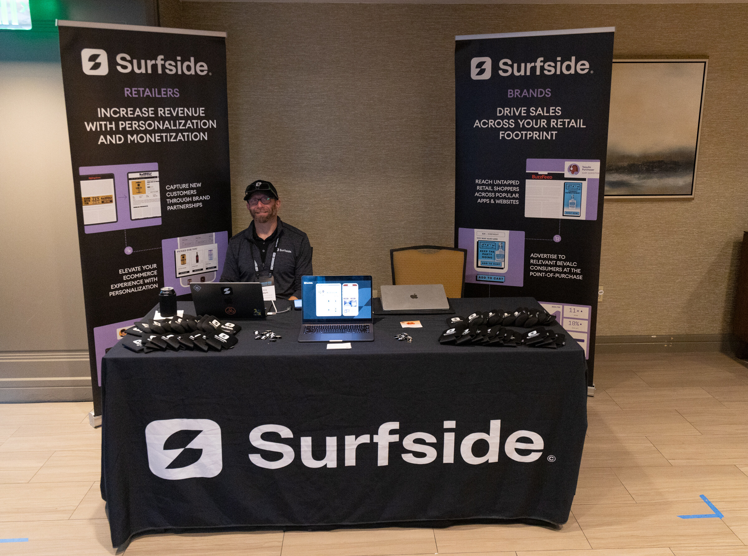 Man seated at a black-draped table with a laptop between two Surfside pull-up banners.