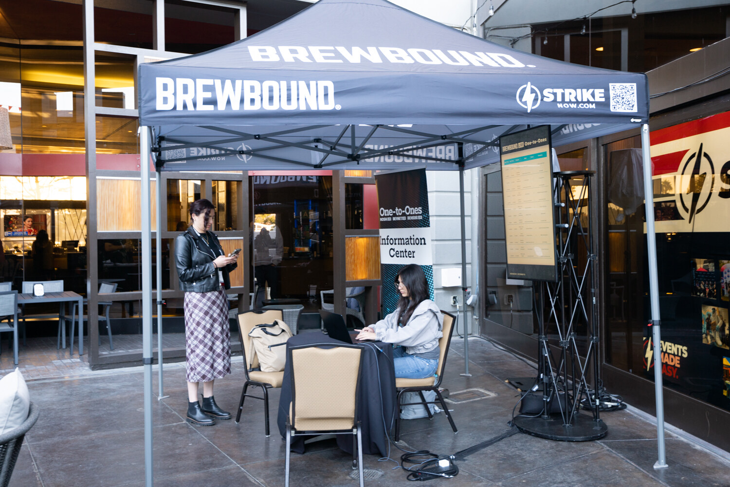 Brewbound canopy tent with a woman seated at a laptop and a woman standing beside a sign reading Information Center.
