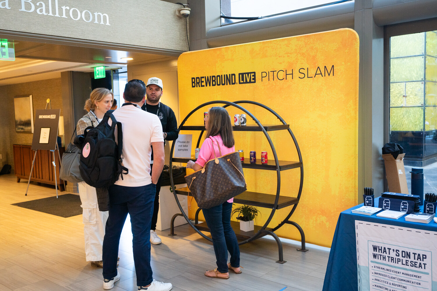 Yellow Brewbound Live Pitch Slam display with a round shelf of cans and attendees standing nearby.