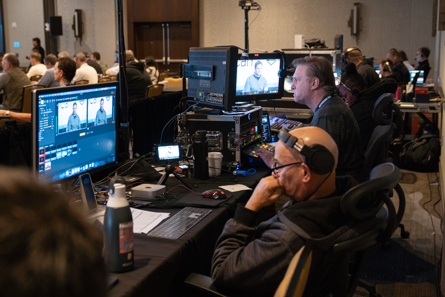 Two men wearing headsets at a video switcher with monitors showing the stage feed.