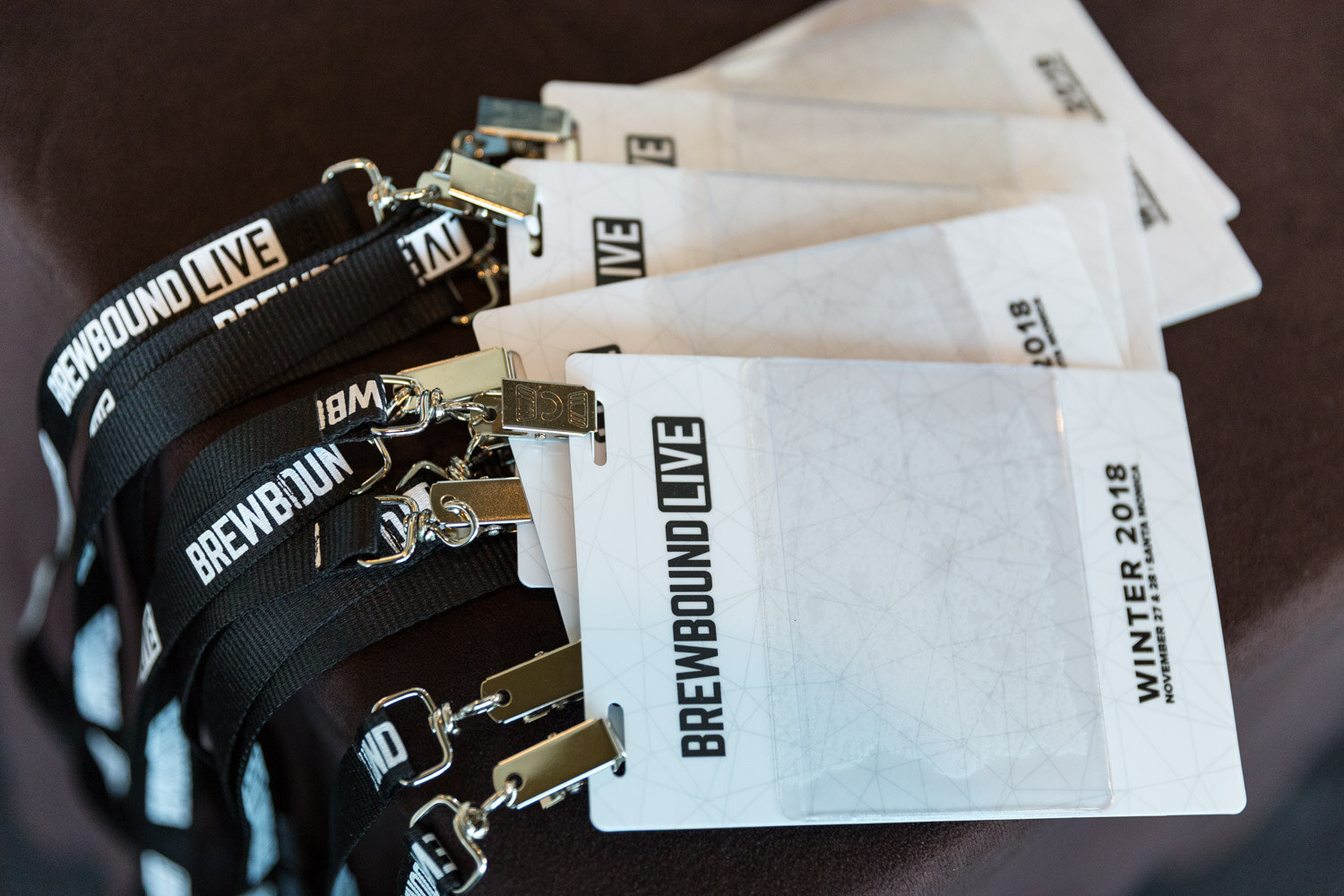 A fan of white conference badges and black Brewbound Live lanyards on a dark tablecloth.