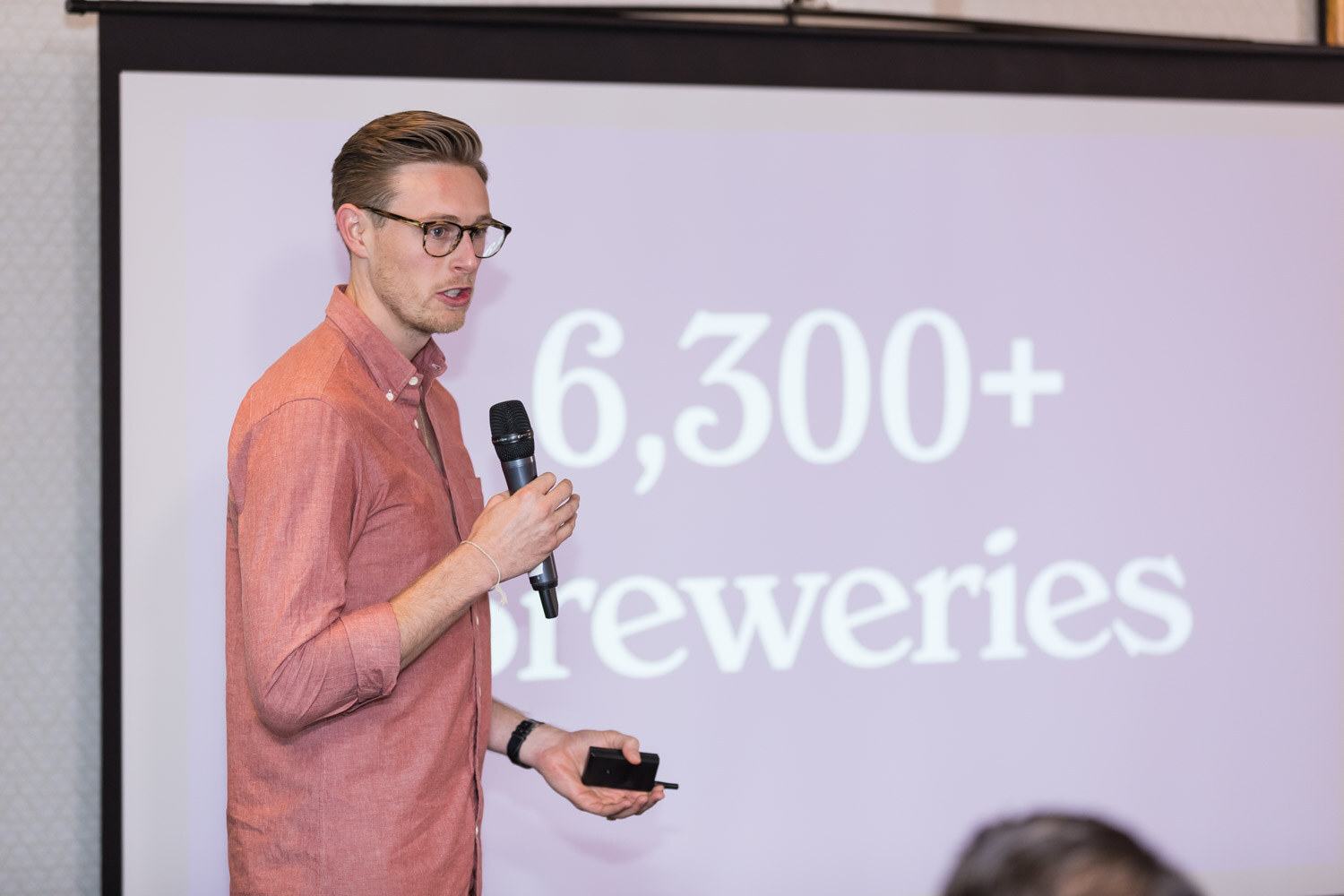 A man with a microphone stands beside a projection screen showing large type that reads 6,300+ breweries.