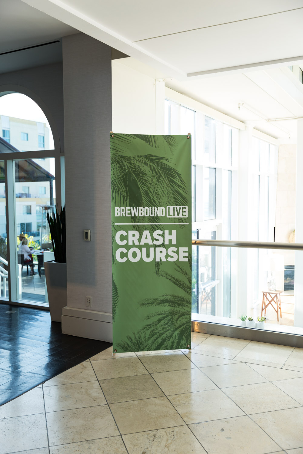 A tall green pop-up banner reading Brewbound Live Crash Course beside large windows.