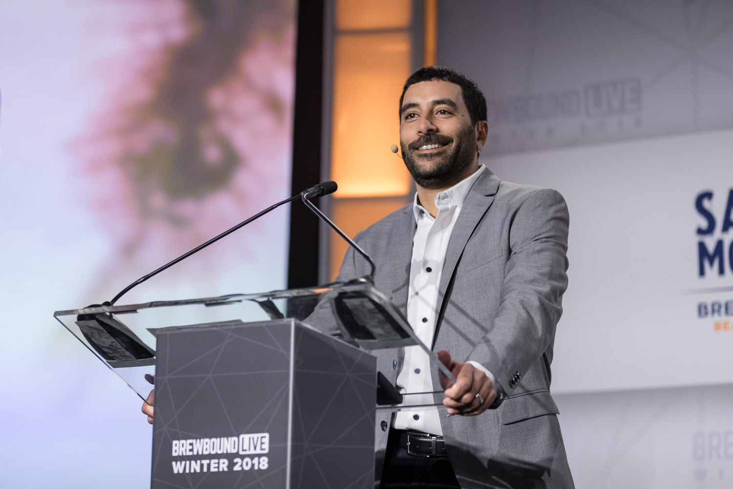 A man in a gray blazer stands at a clear podium marked Brewbound Live Winter 2018.