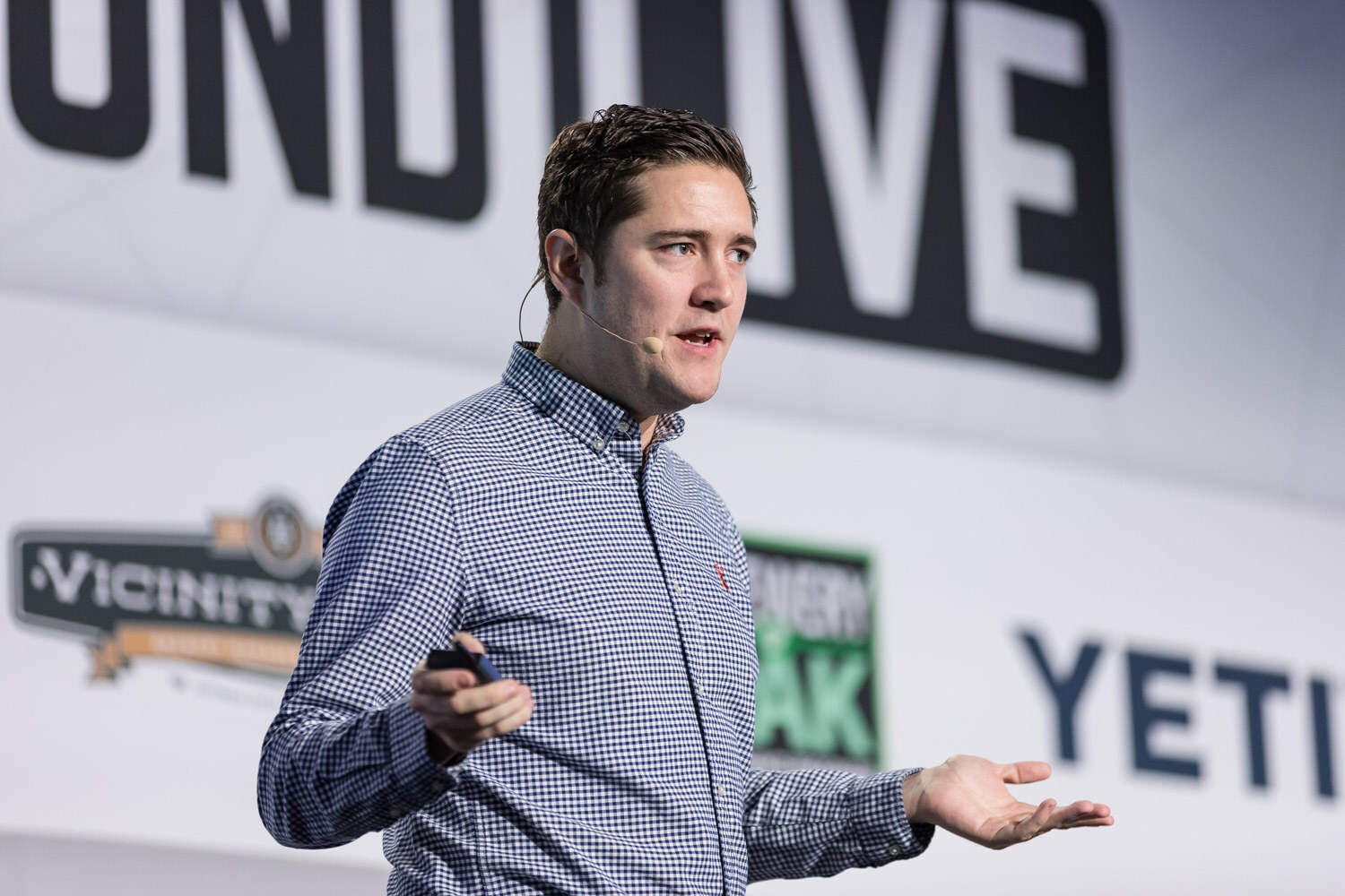 A man in a blue checked shirt with a headset microphone gestures in front of a Brewbound Live and YETI backdrop.